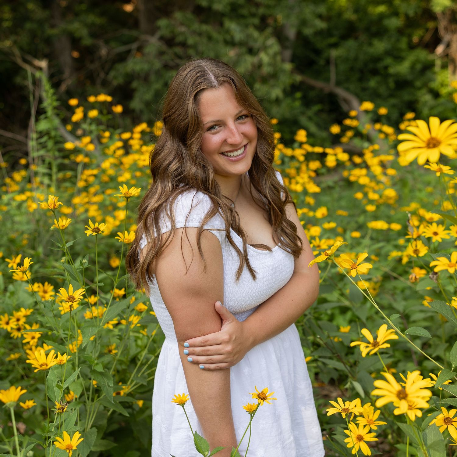A person in white poses among vibrant yellow flowers in a garden setting.