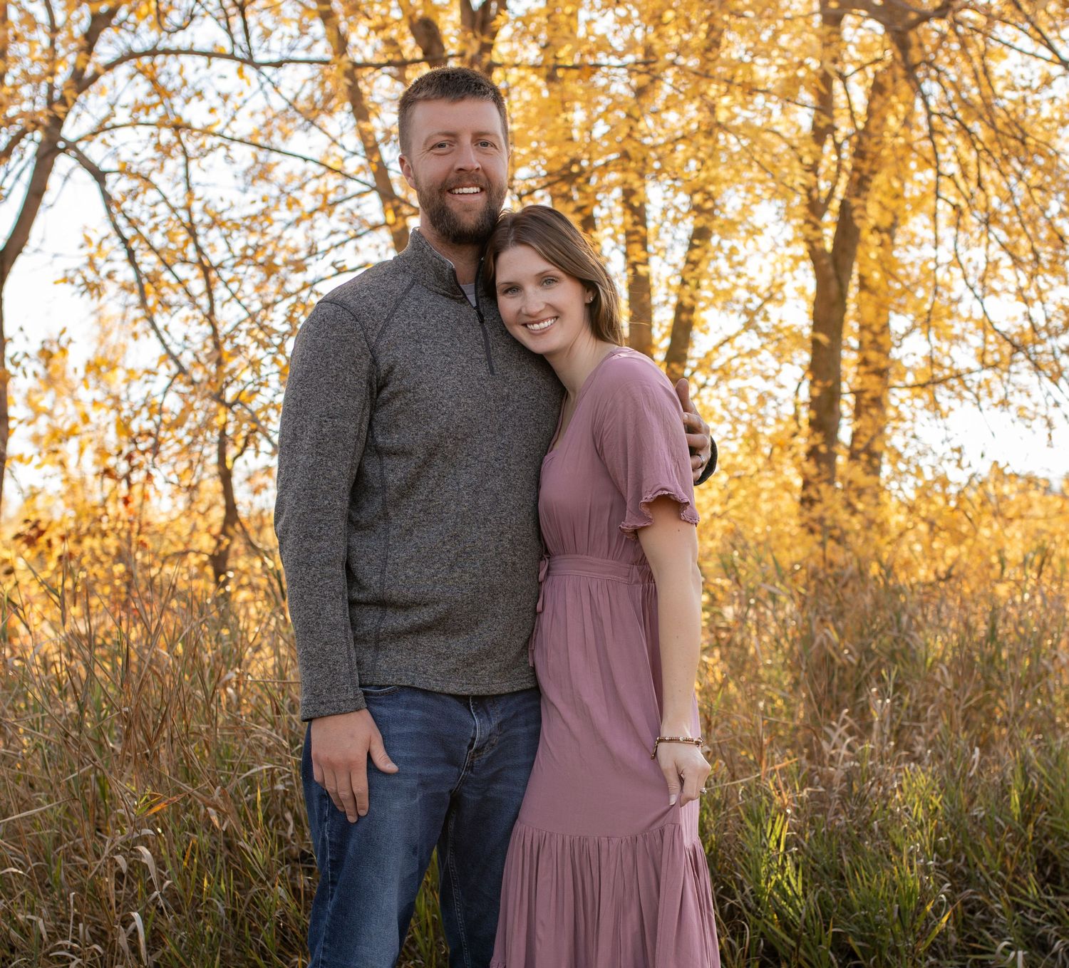 A couple poses together in an autumn field at golden hour.