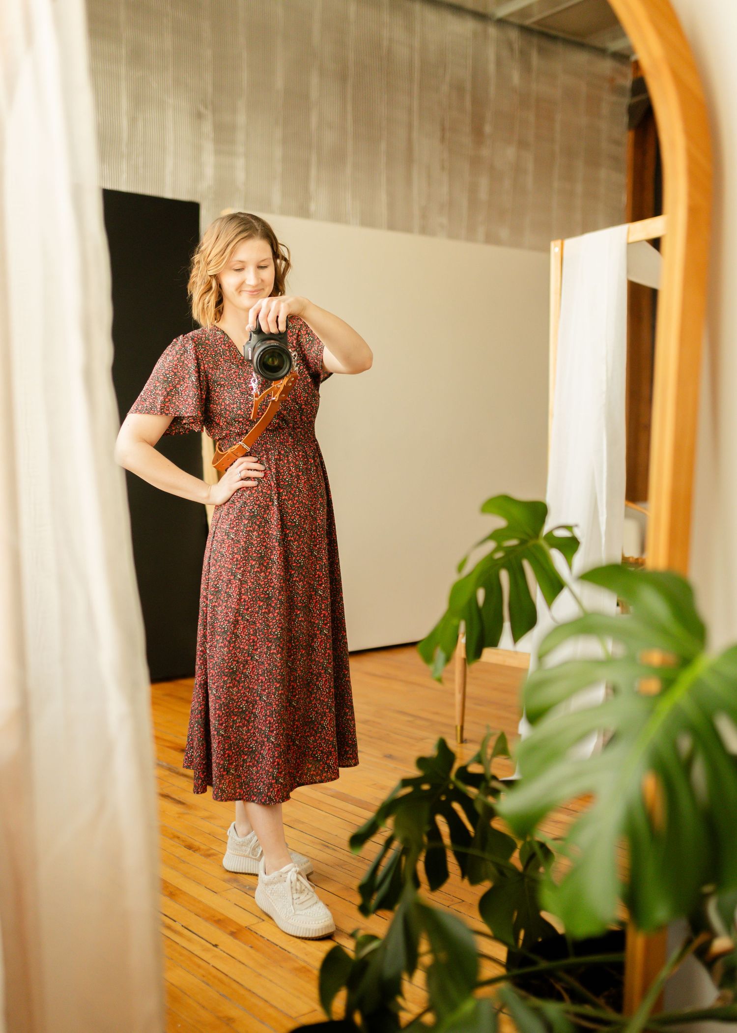 A floral dress photoshoot in an indoor studio space with monstera plants and white curtains.
