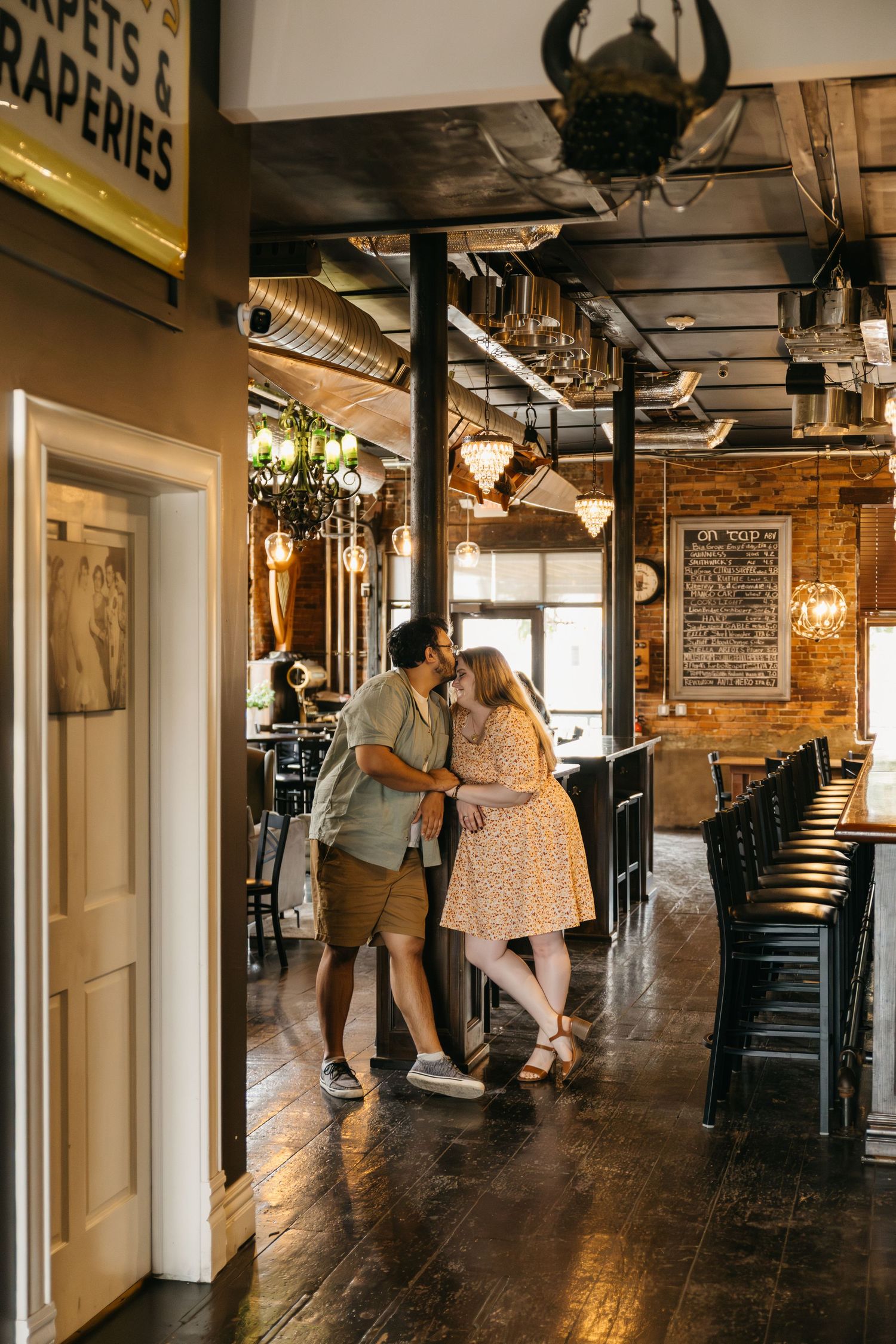 A romantic engagement photo session in a rustic industrial hallway with exposed brick walls and warm lighting.