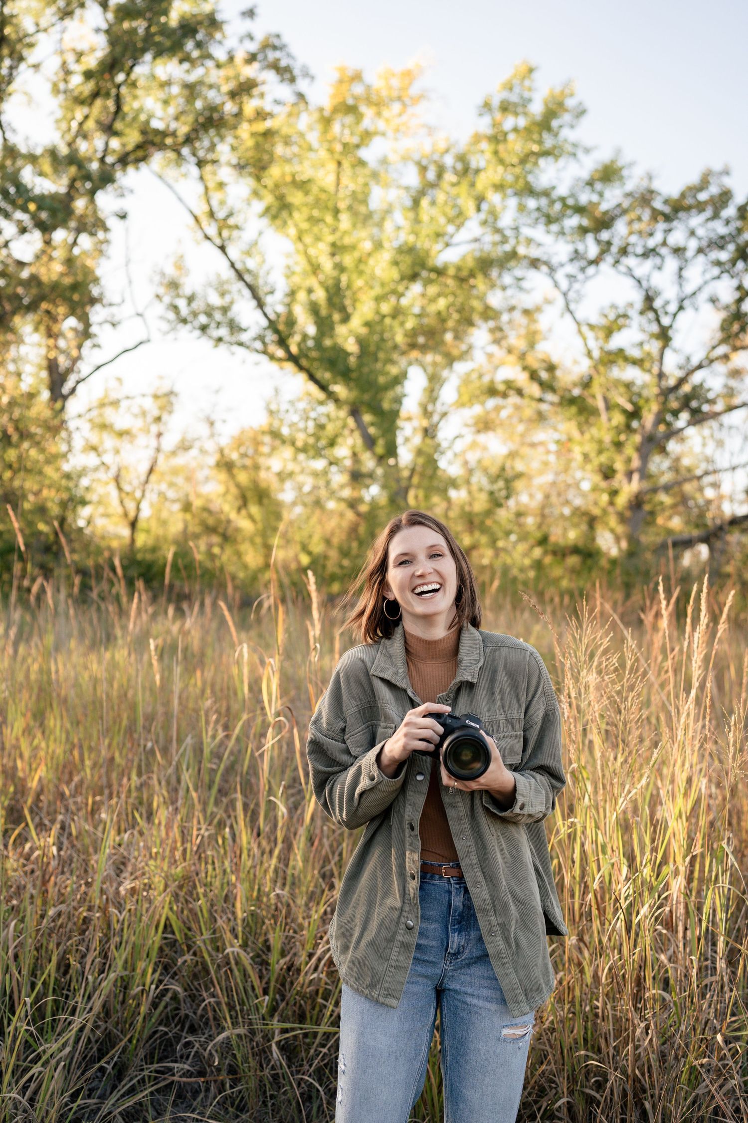 A joyful outdoor photography session in a sunlit field with tall grass and trees.