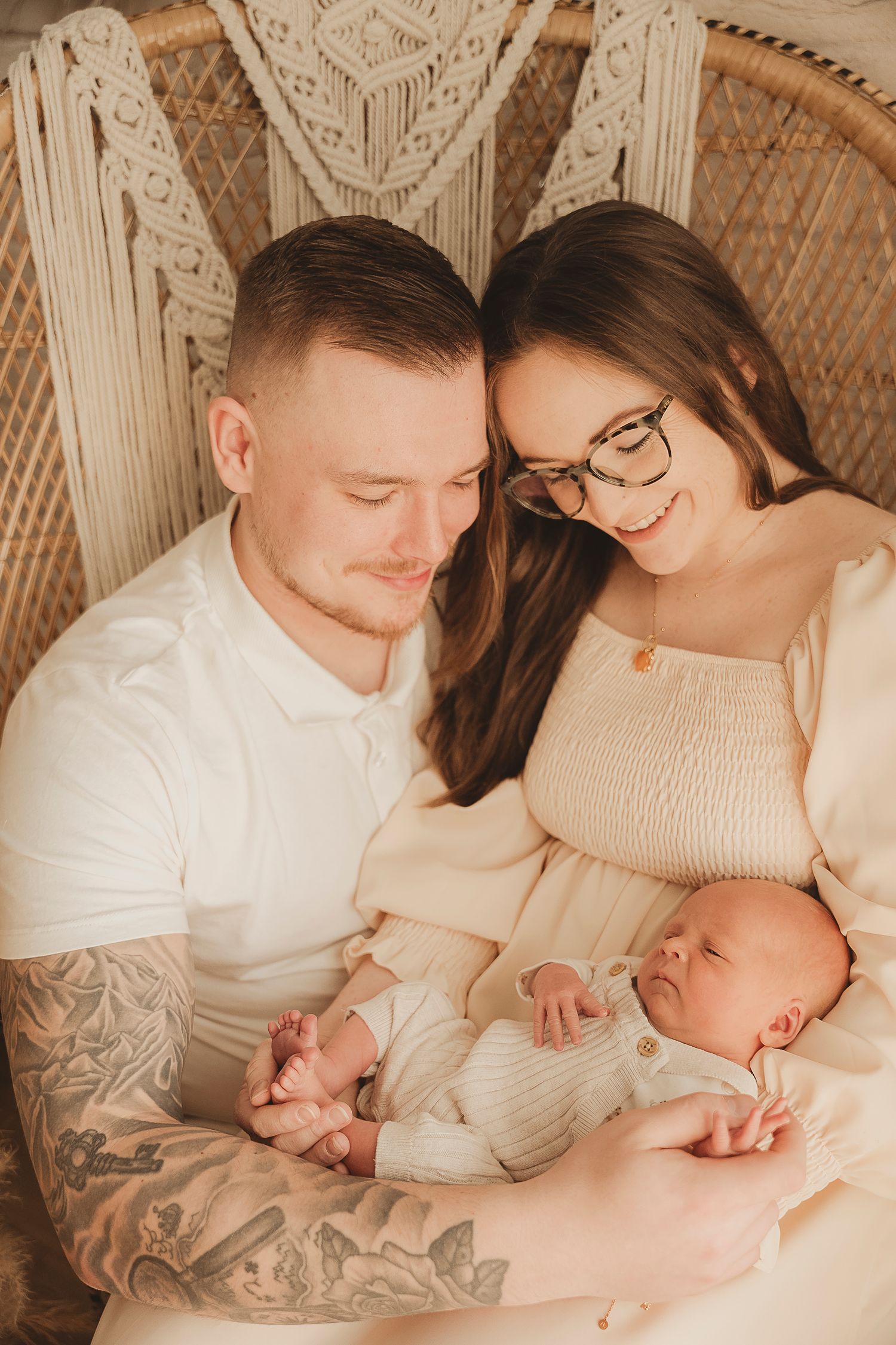 Intimate family moment captured in a wicker chair with parents looking lovingly at their newborn.
