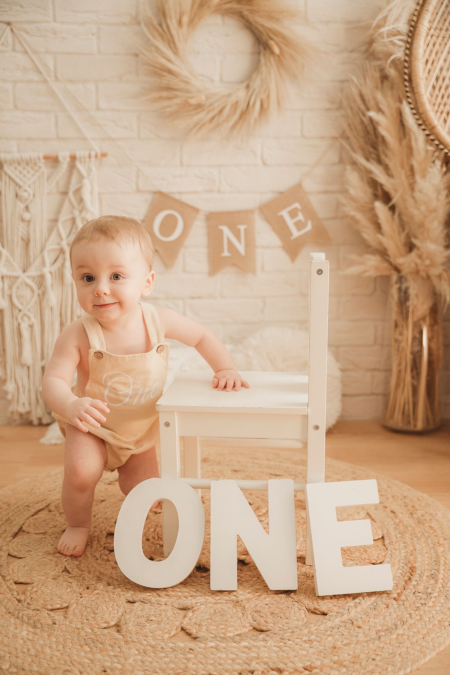 Baby's first birthday setup with ONE banner and decorative pampas grass against white brick wall.