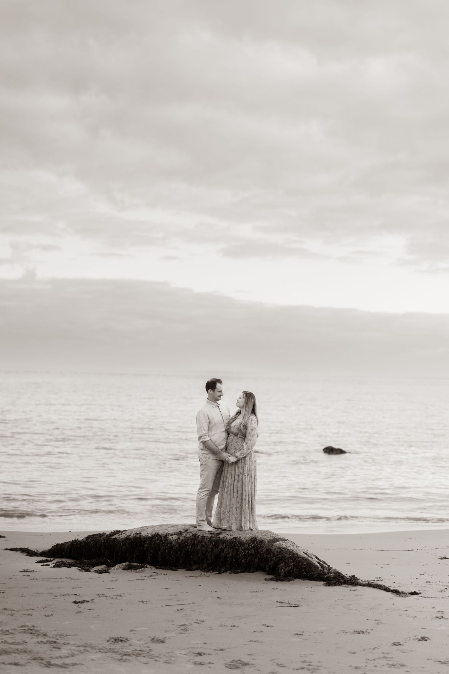 Sweeping cinematic portrait of couple holding hands facing each other in front of the ocean during their engagement session