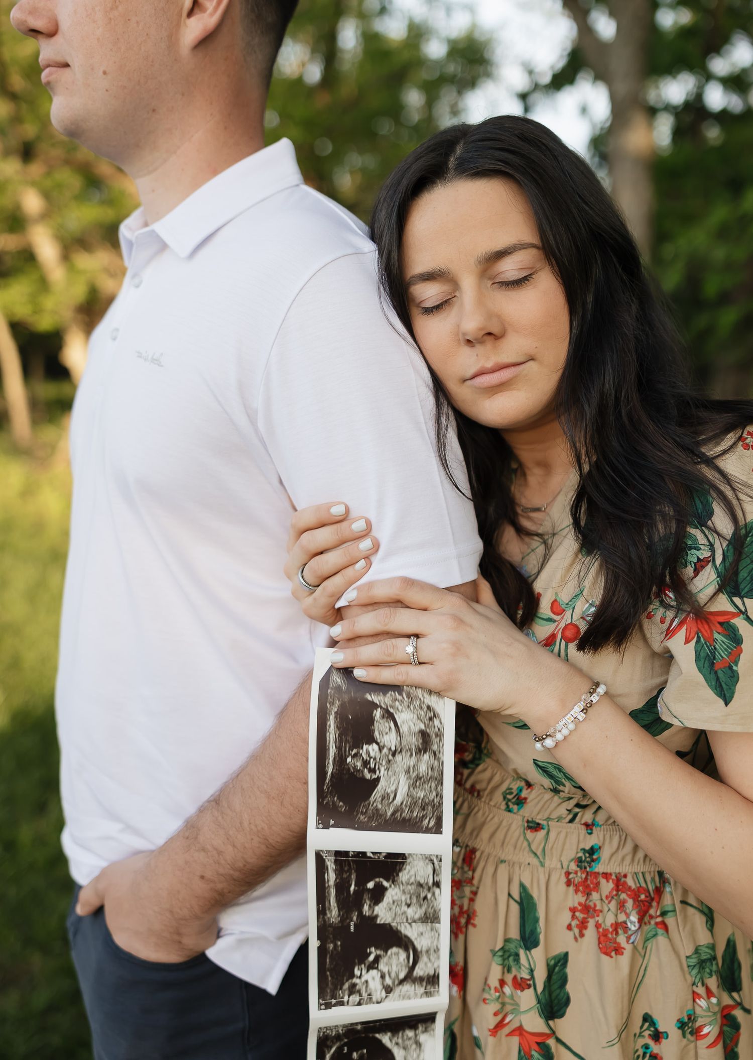 mom resting her head on her husbands arm with her eyes closed holding a sonogram of their growing baby