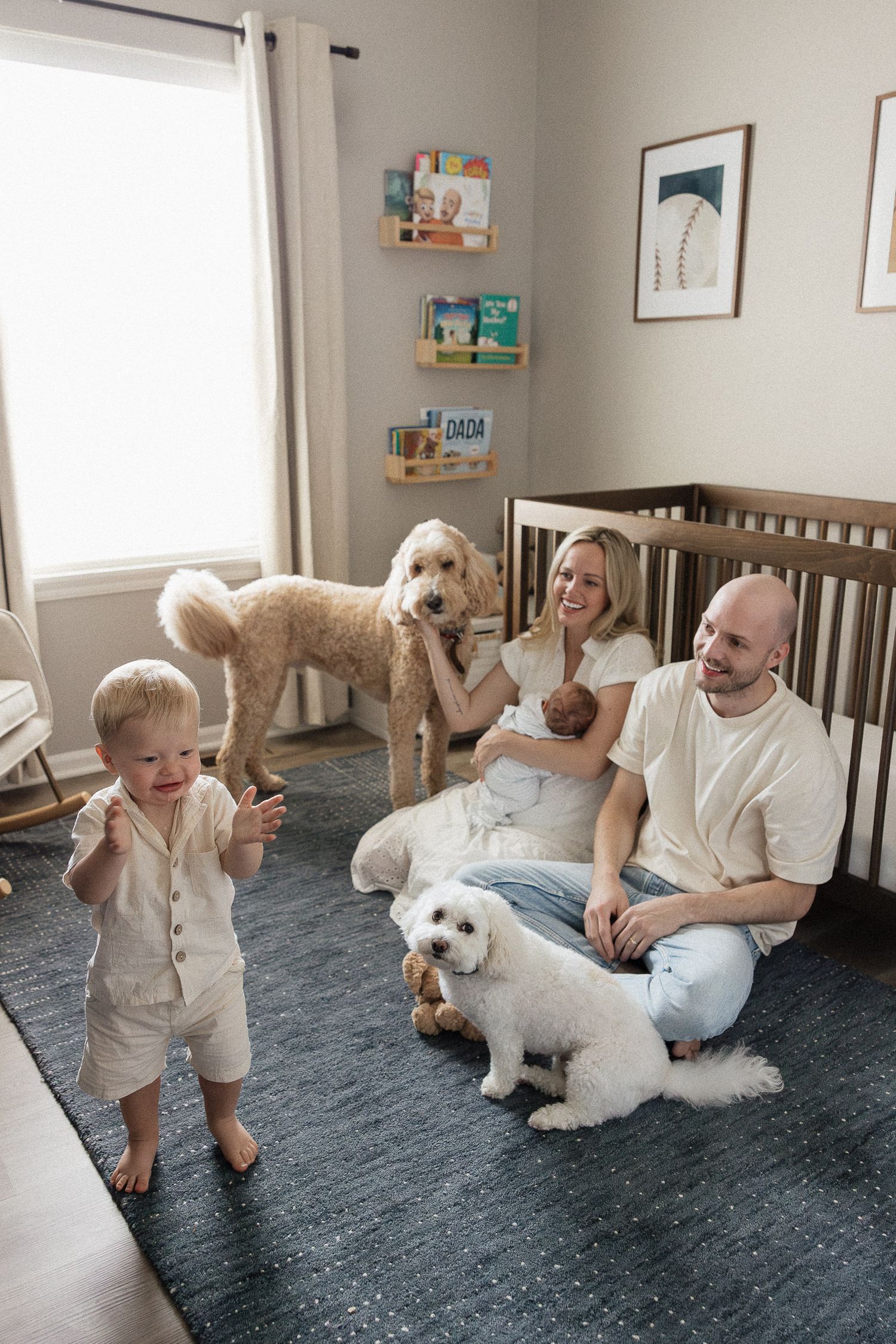 family of four sitting on nursery floor singing as toddler dances around two dogs photographer overland park ks