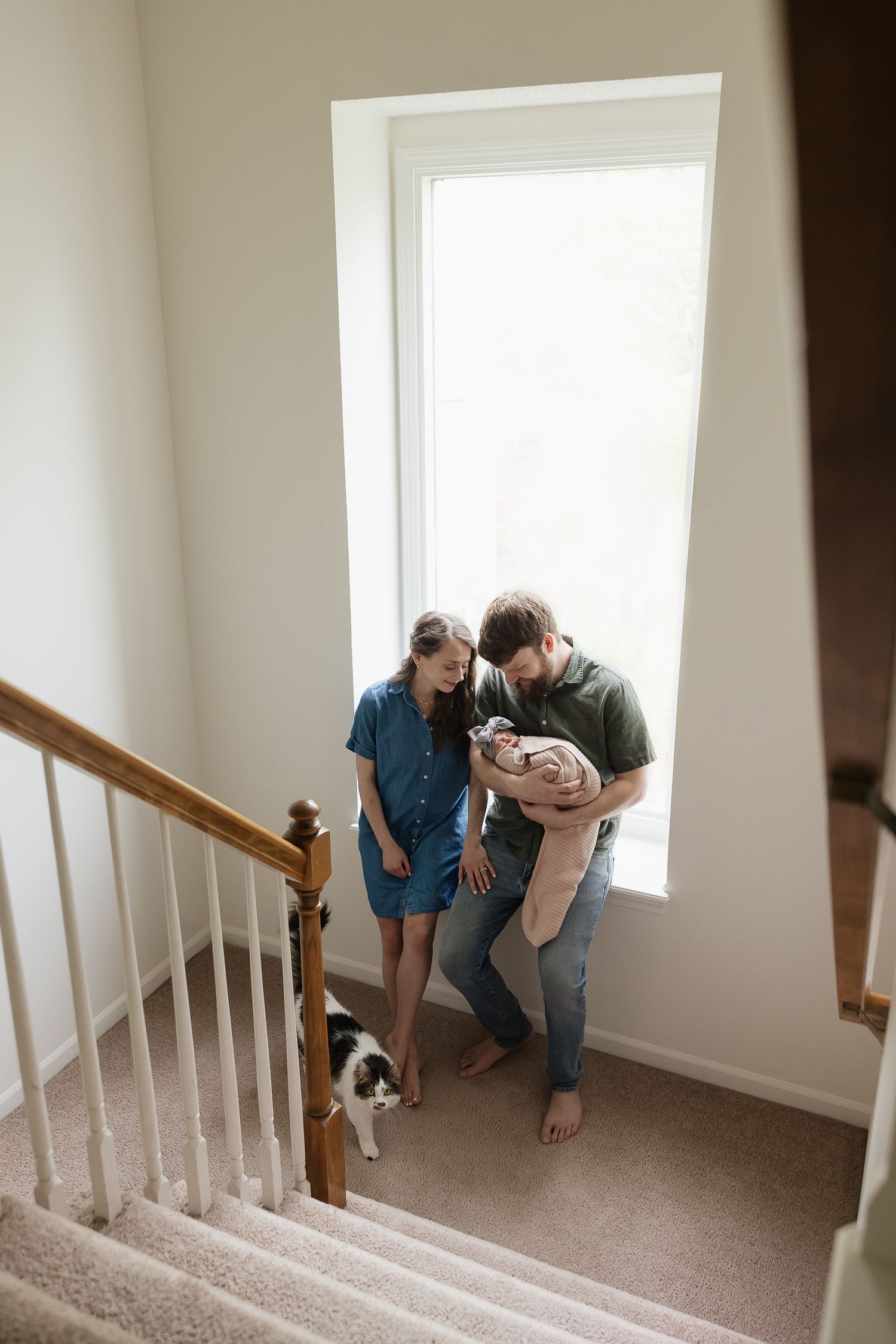 Kansas City Newborn Photographer documenting mom and dad with baby sitting on stairway with cat