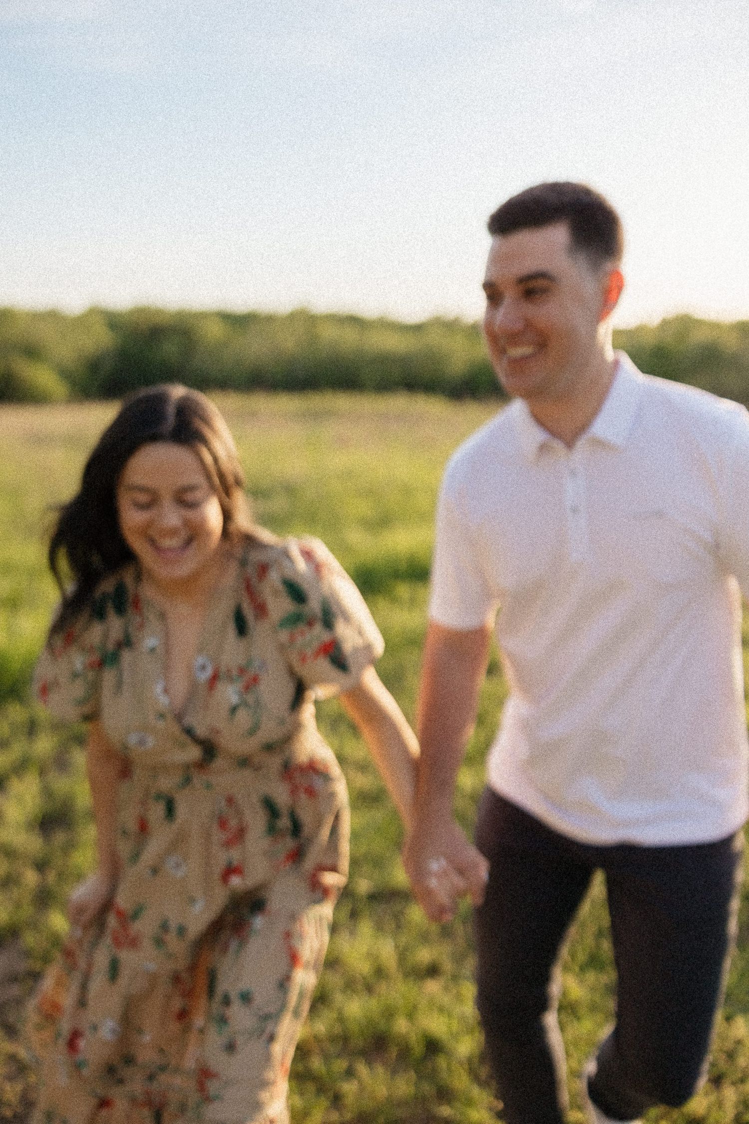 blurry and grainy photo of couple holding hands and running in a prairie grass field with blue skies at ernie miller park