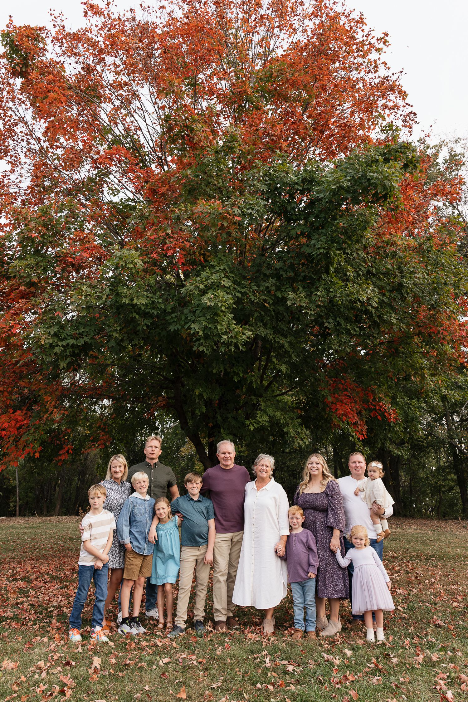 extended family group photo of everyone smiling at shawnee mission park with beautiful red leaves changing behind family