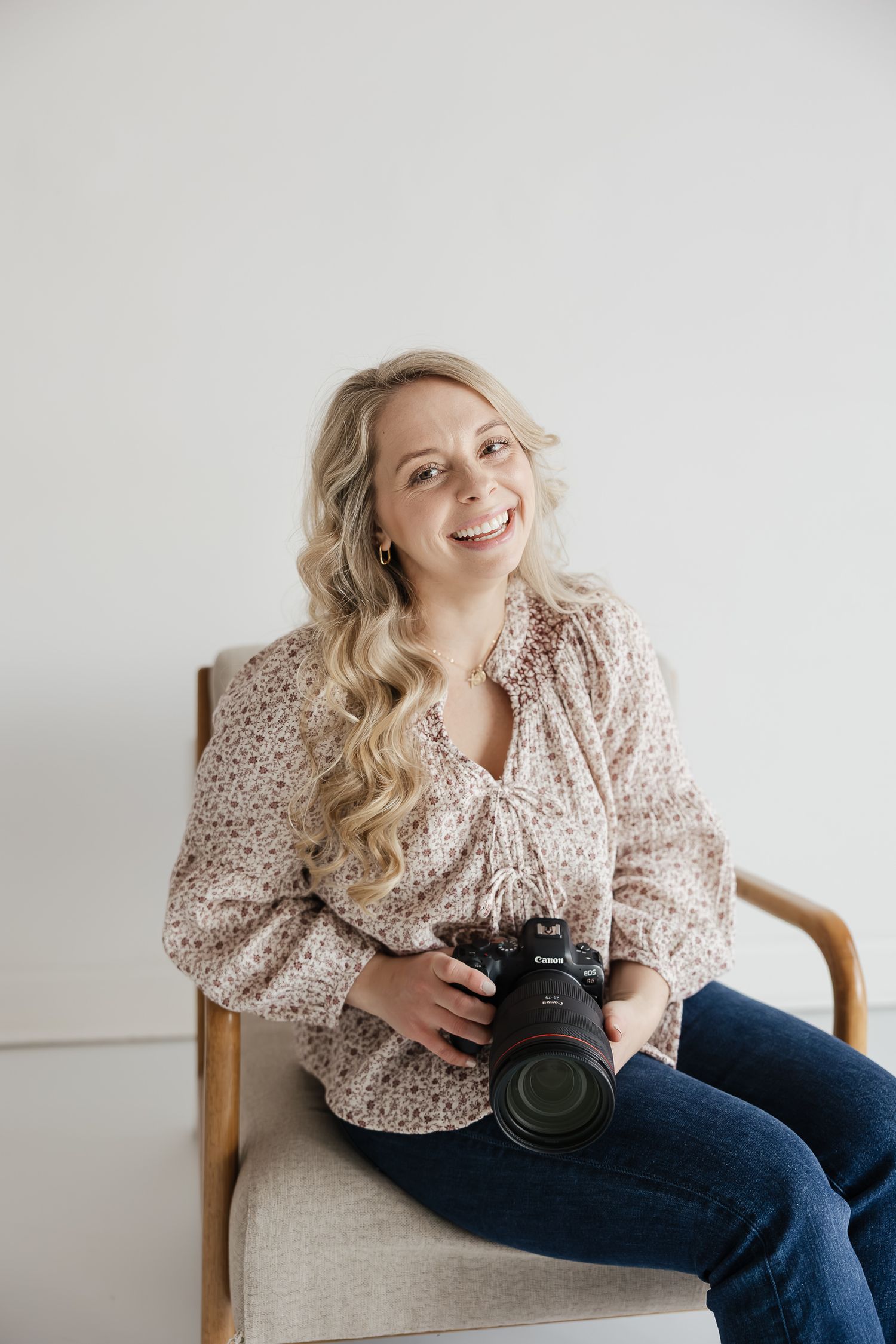 headshot image of kansas city newborn photographer holding camera sitting in chair smiling