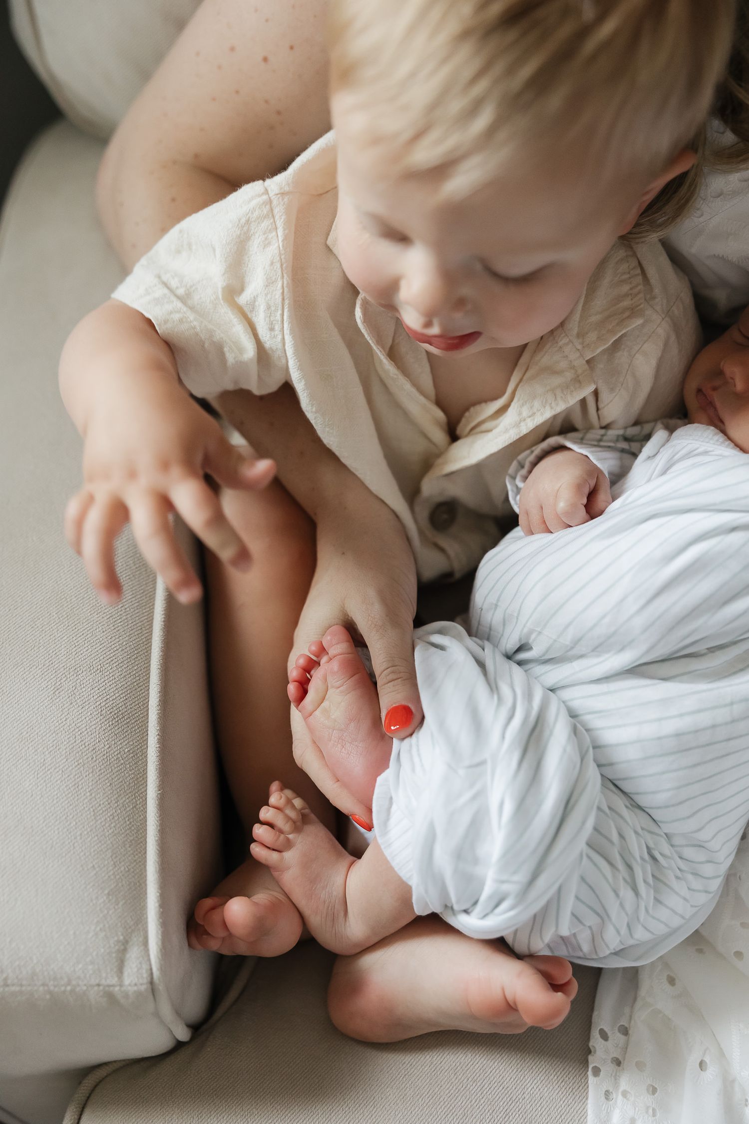 photographer overland park ks captures toddler sitting on moms lap in a rocking chair while pointing to baby brothers little toes