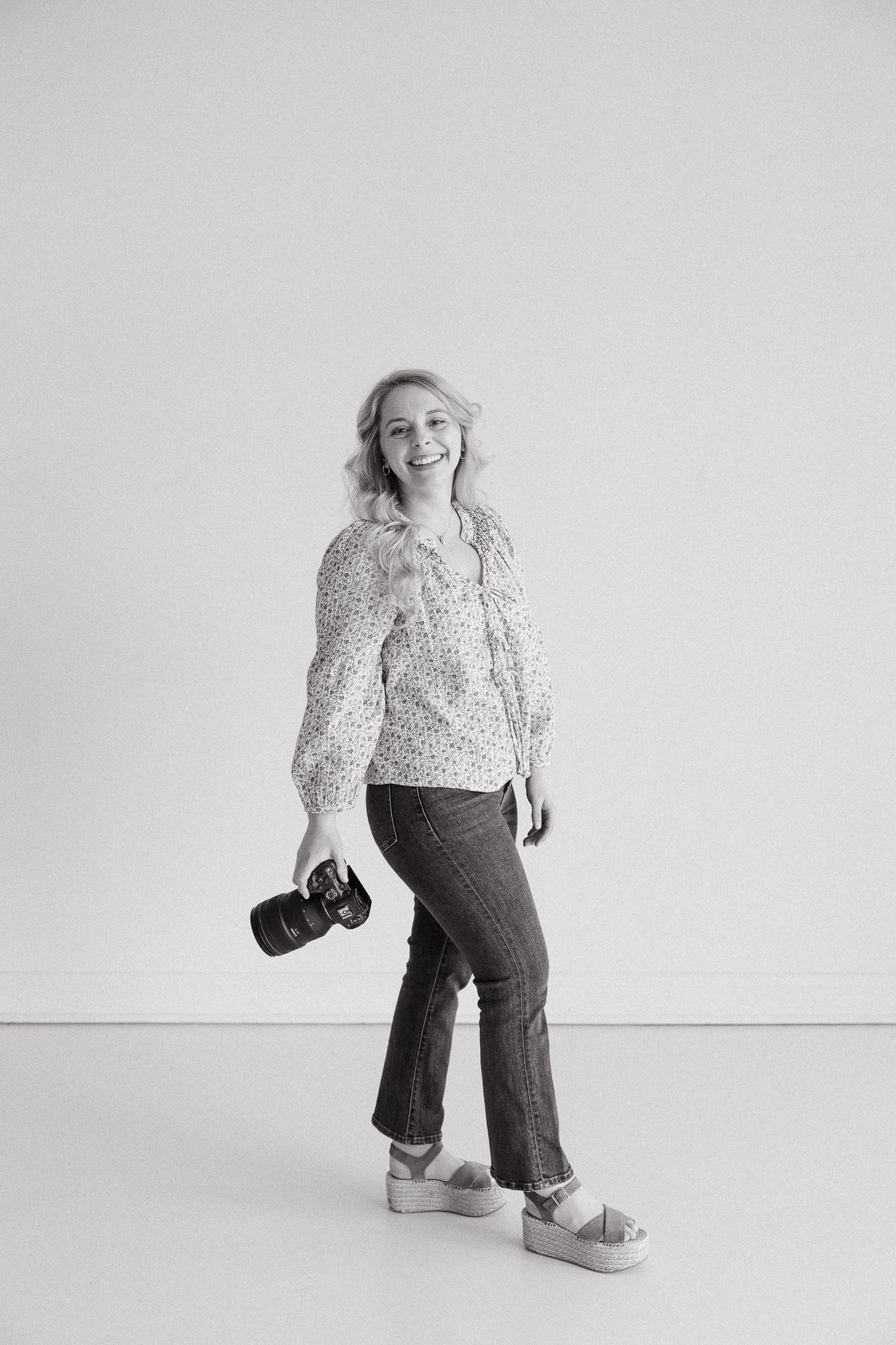kansas city family photographer holding her camera in a blank studio space smiling