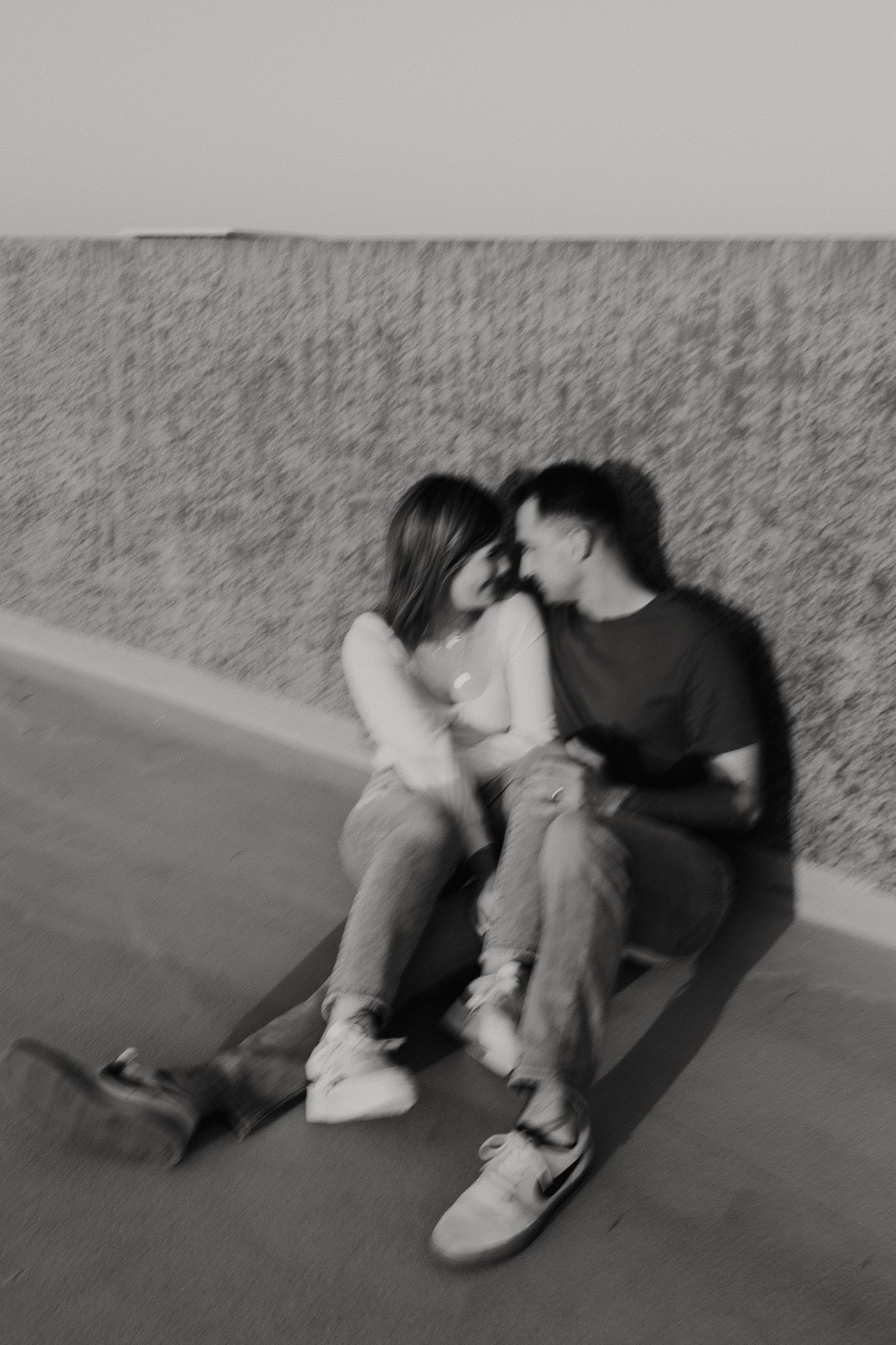 black and white of couple sitting against stone wall in direct sun on parking garage rooftop