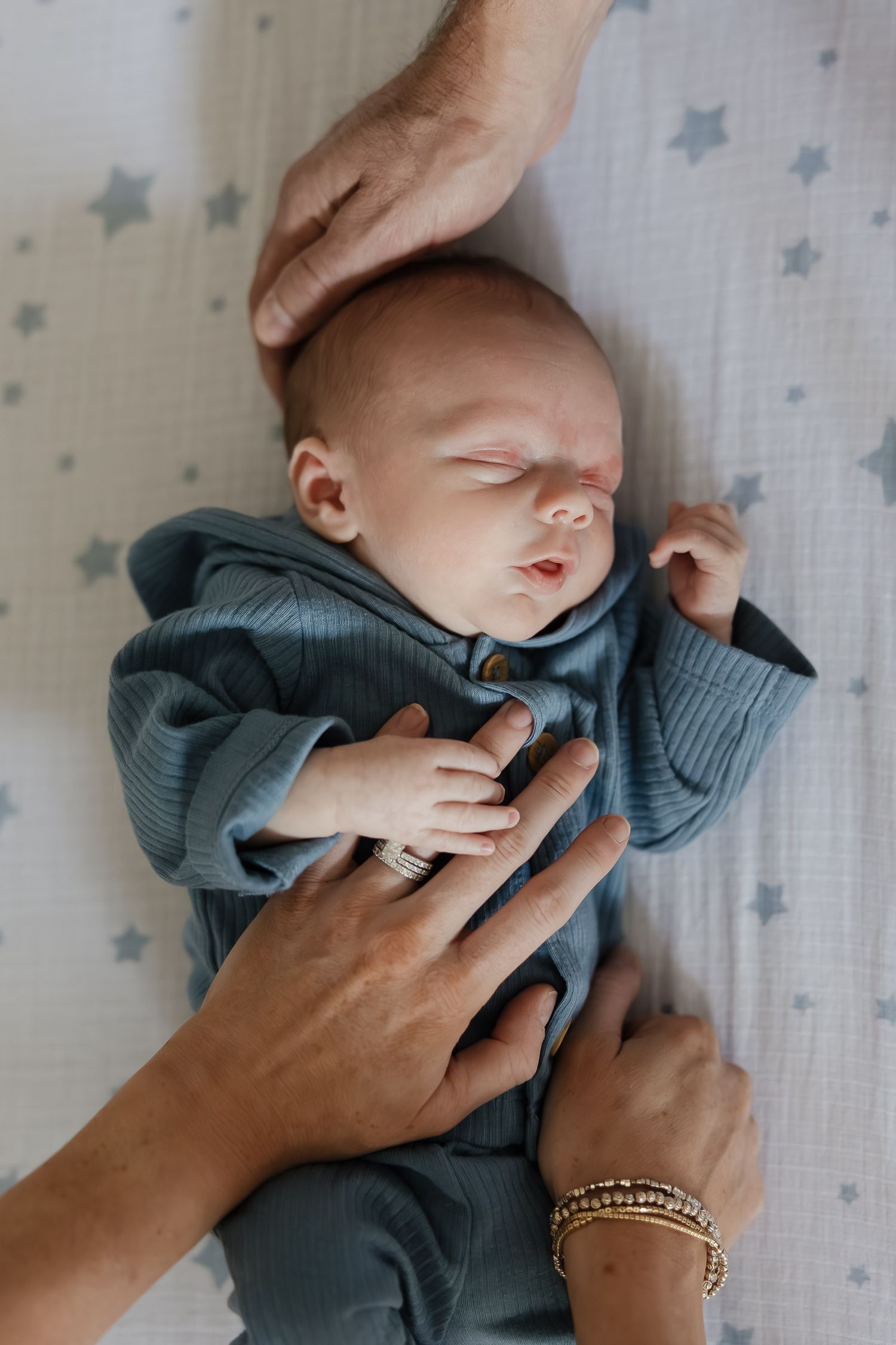 mom and dad putting both of their hands on a newborn baby boy lying in his crib while kansas city newborn photographer takes photo