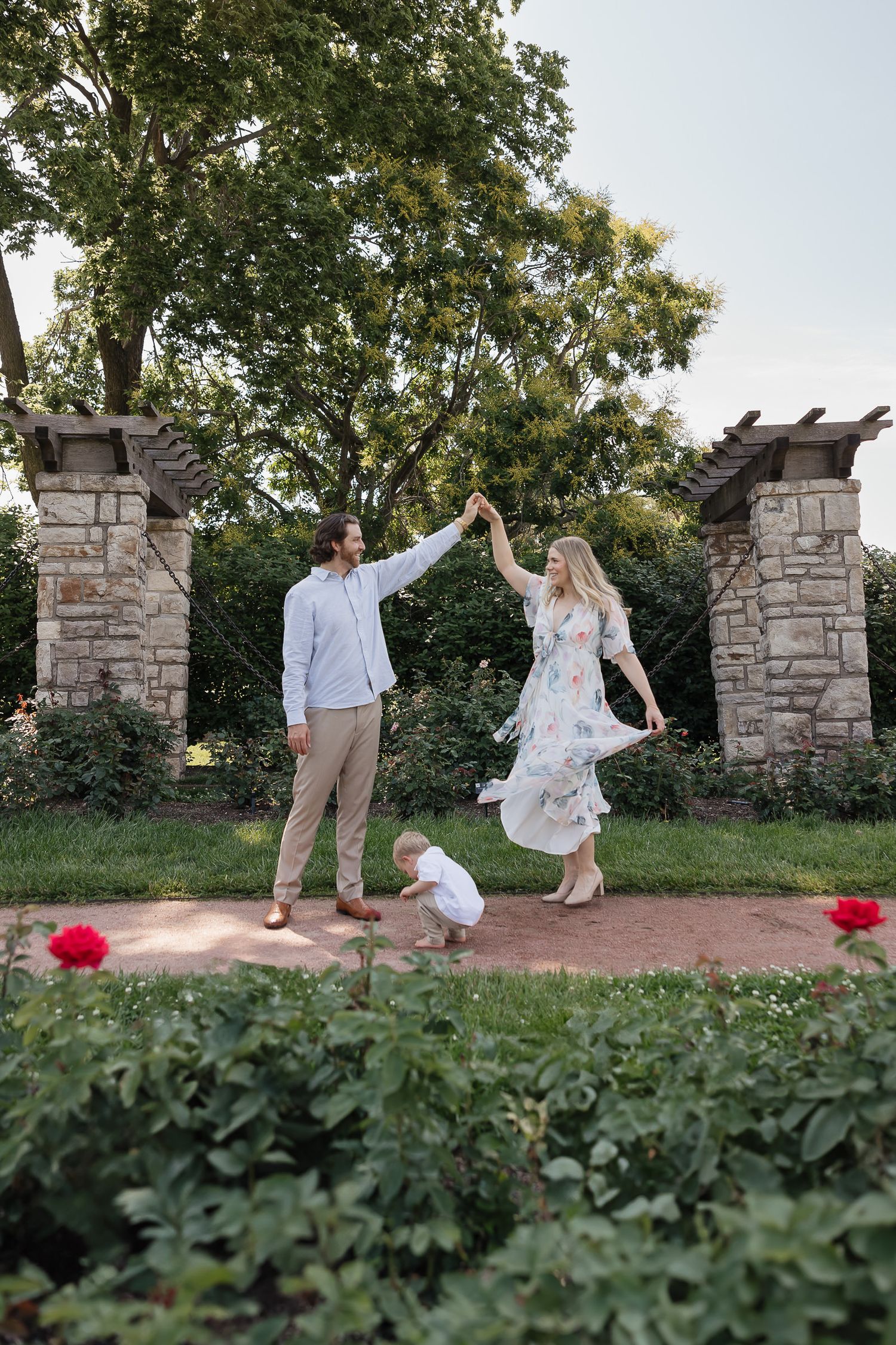 mom and dad dance in kansas city loose park rose garden while son plays in dirt between them