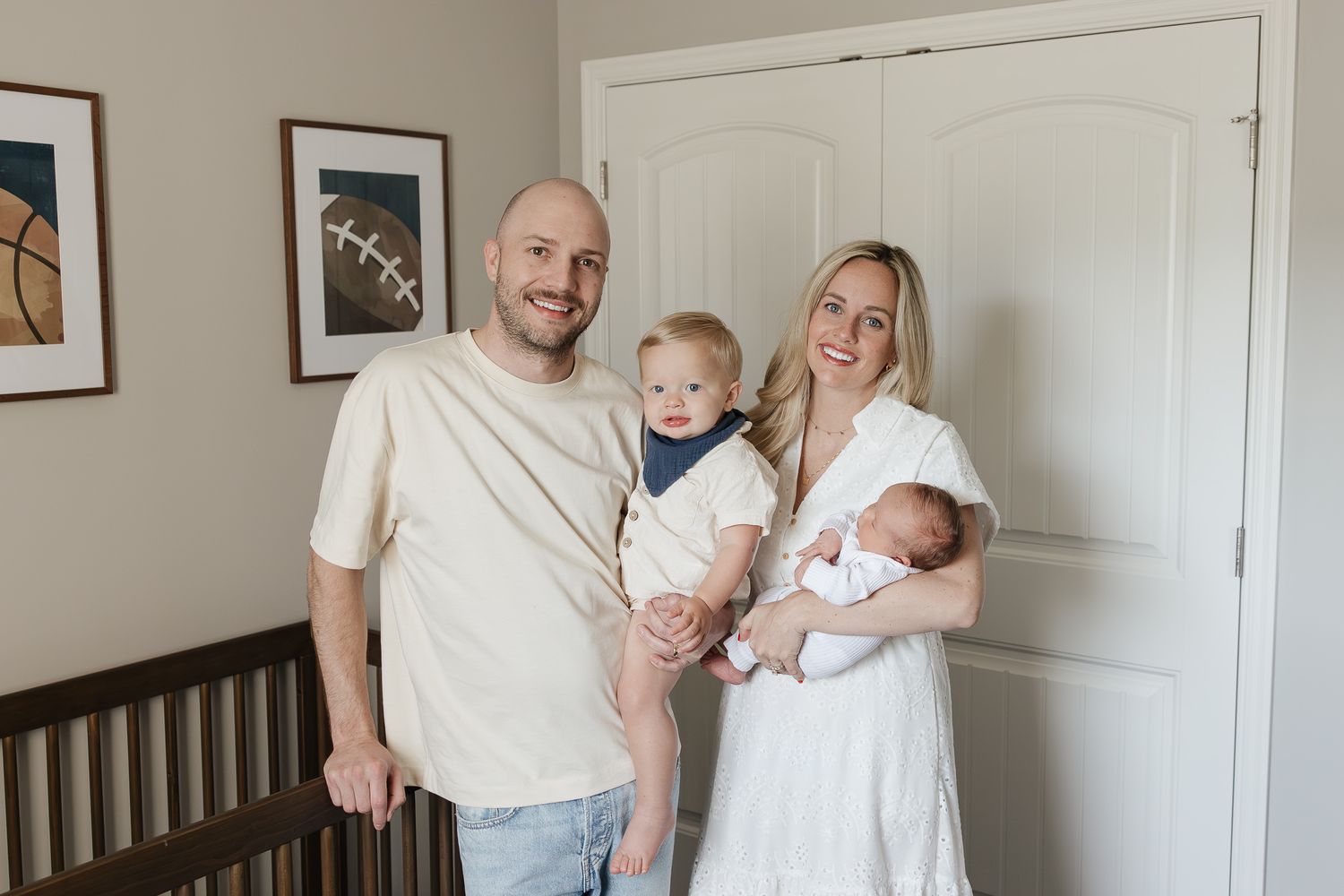 family of four smiling at camera in baby's nursery with sports photos as decoration
