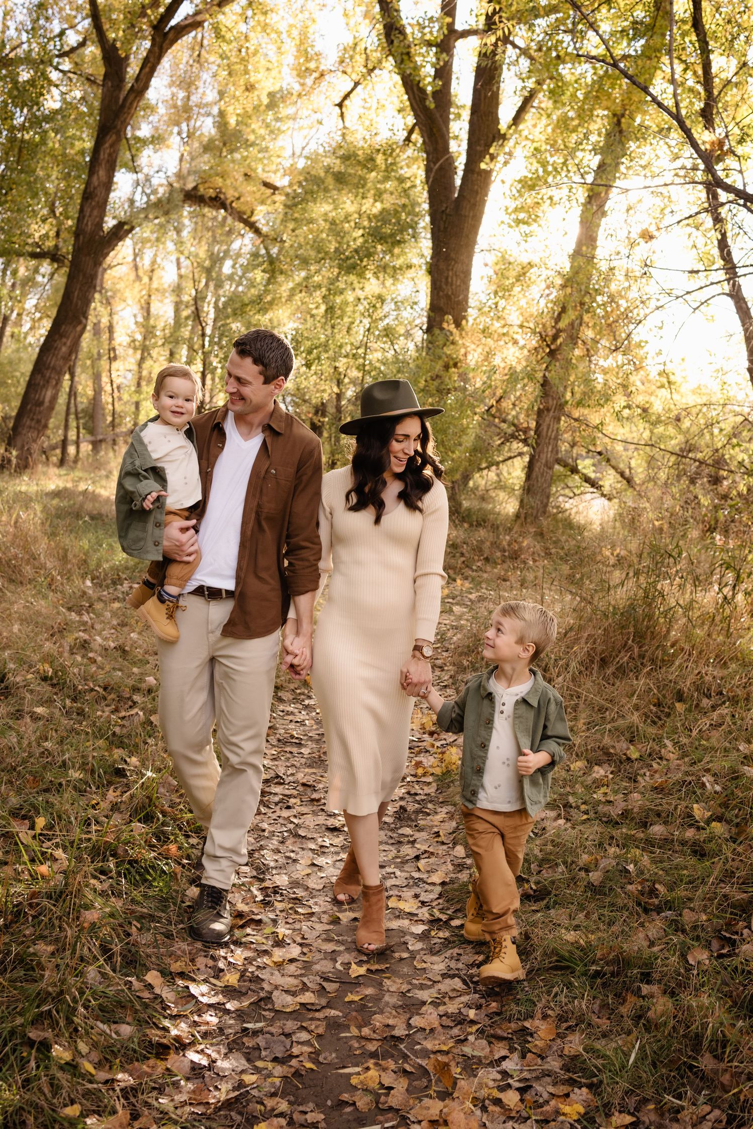Family of four walking on a leaf-covered path in autumn woods, parents holding hands with young children Yellowstone river billings mt