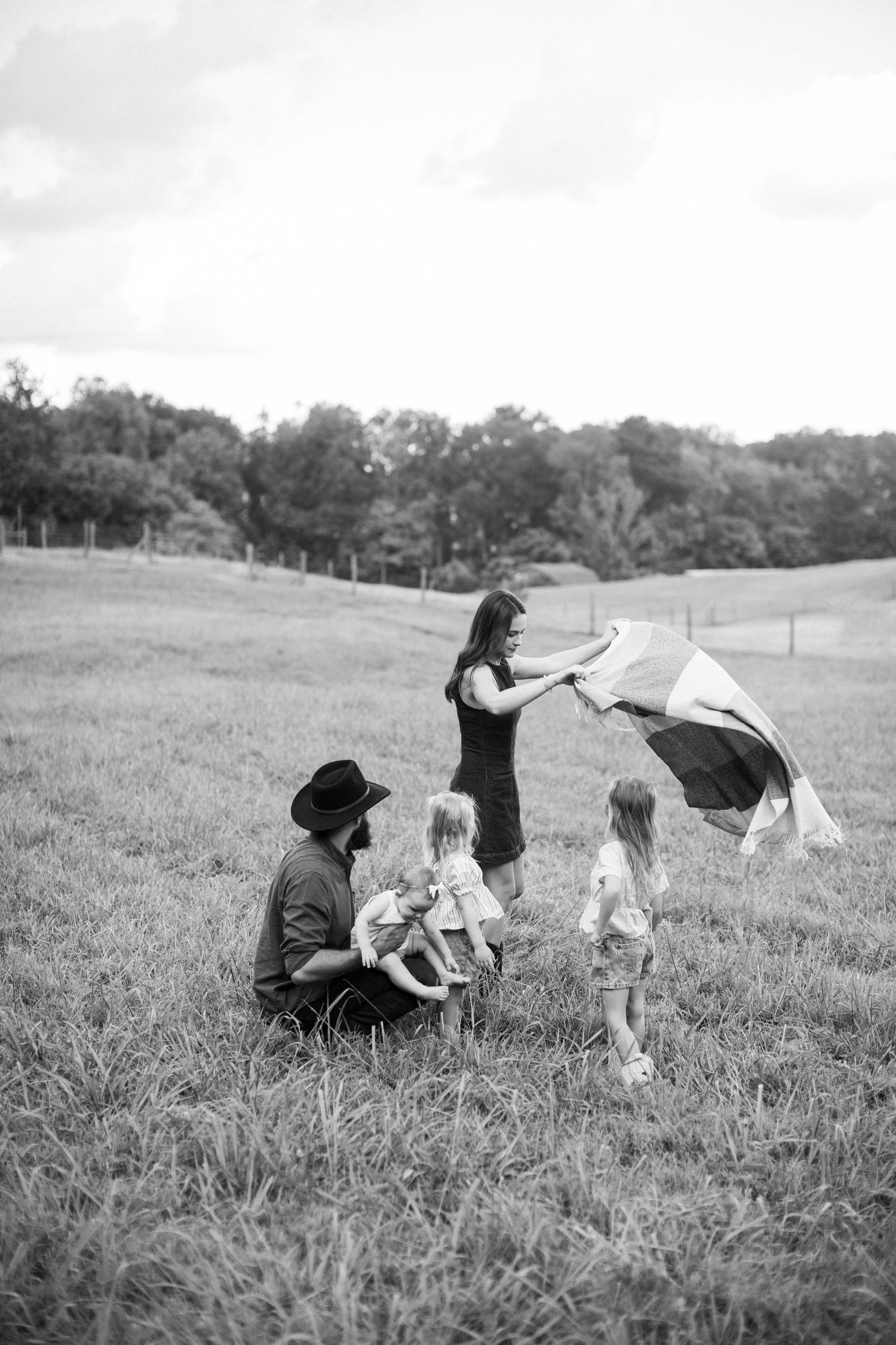 Black and white family photo setting up a picnic together in an open grassy meadow.