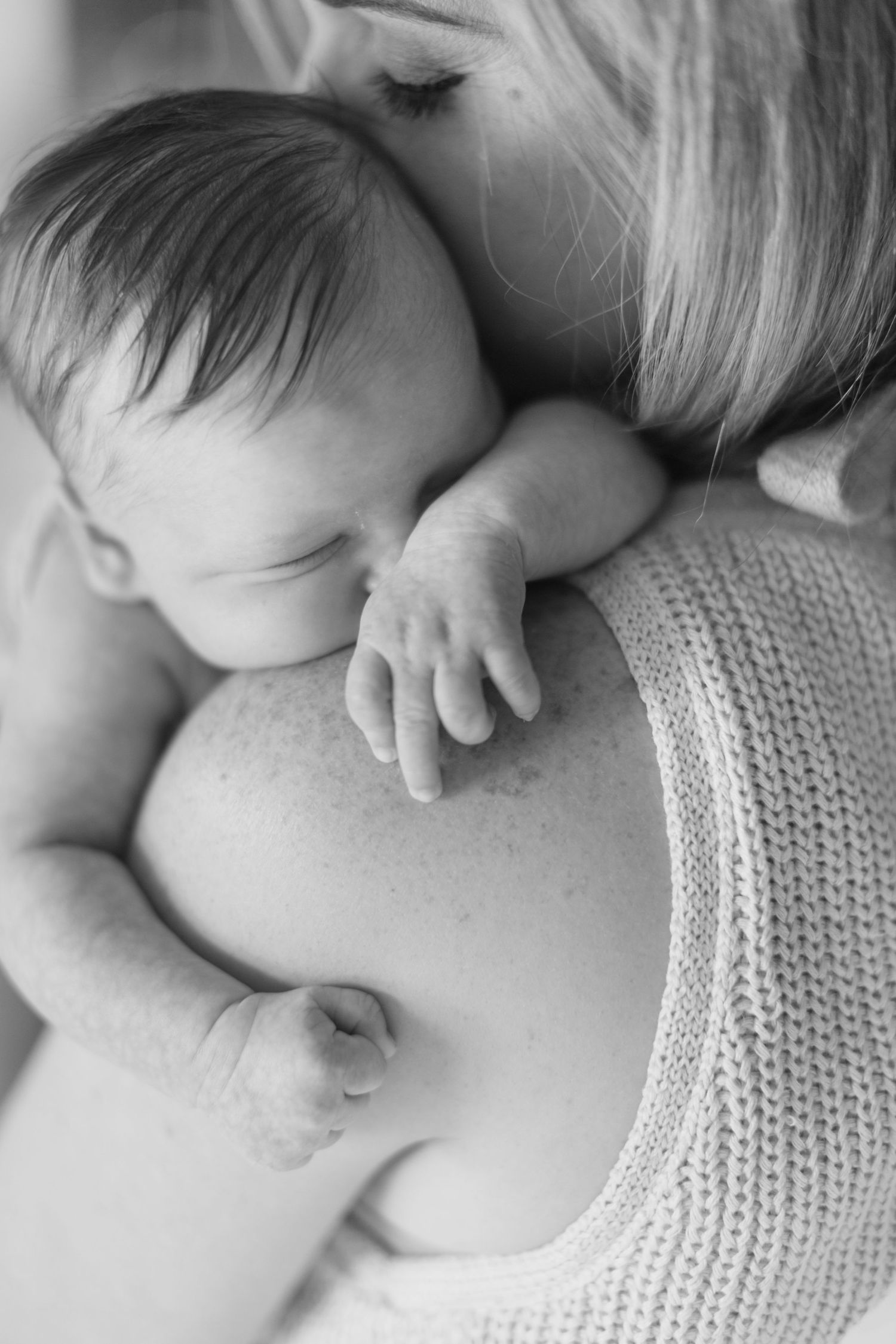 Black and white close-up of a sleeping newborn baby cradled against mother's shoulder.