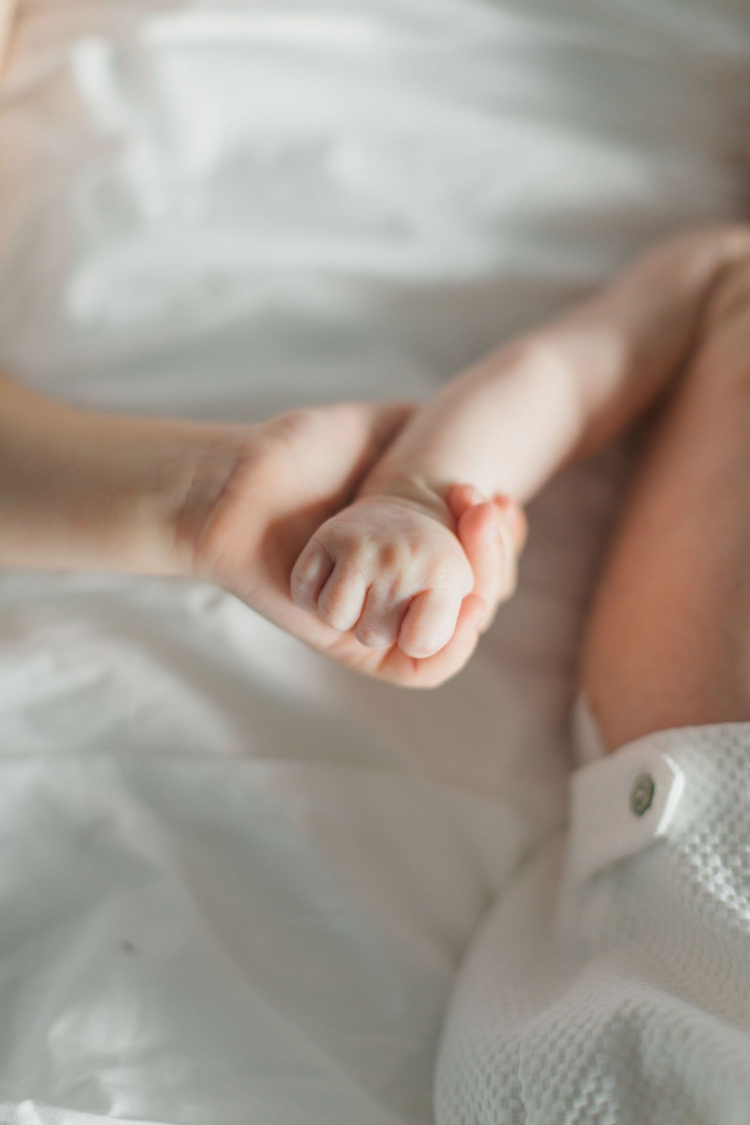 A mother gently holds her newborn baby's tiny hand on a soft white blanket.
