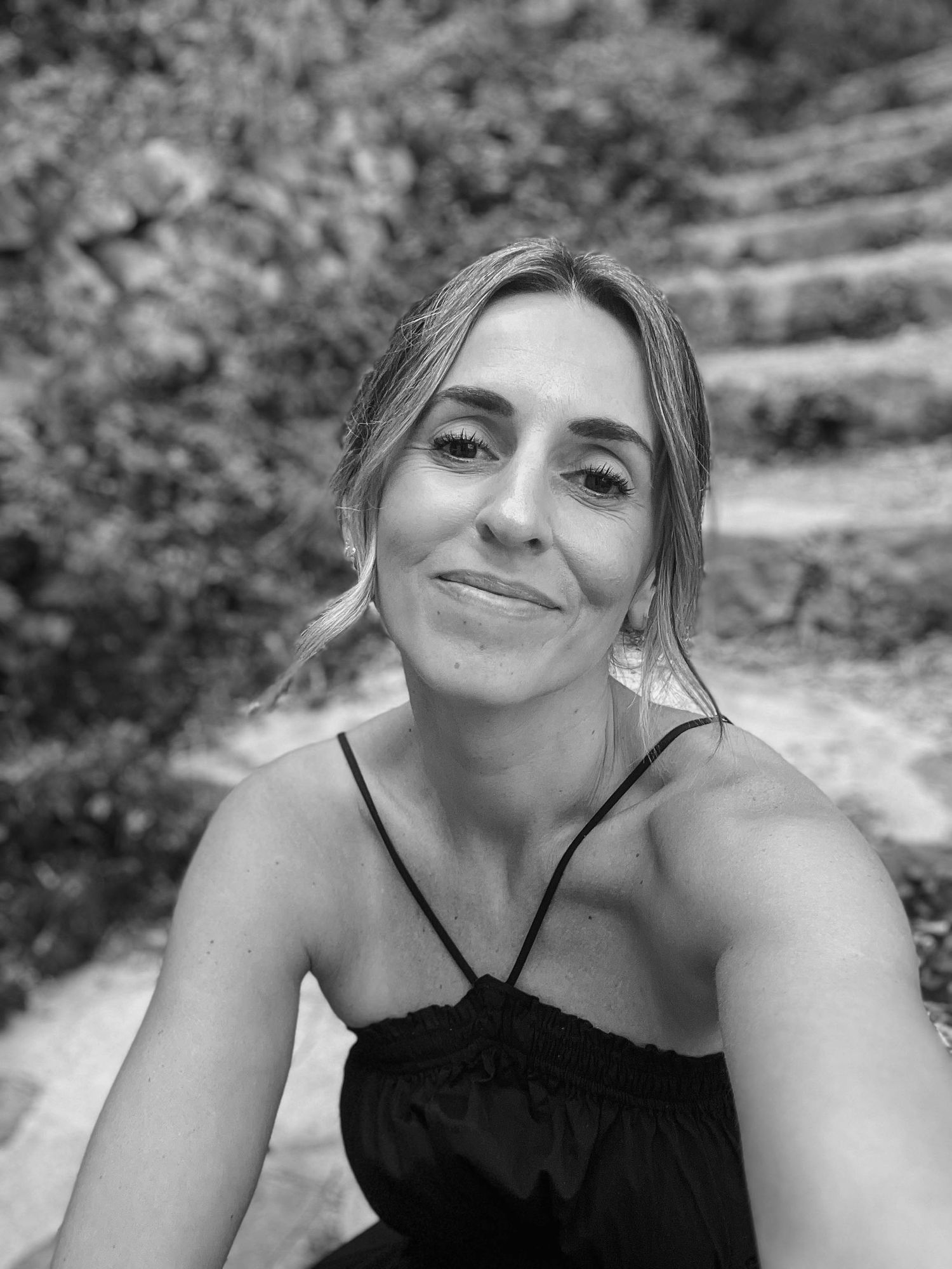 Black and white close-up portrait of a smiling woman in a black dress on stone steps.