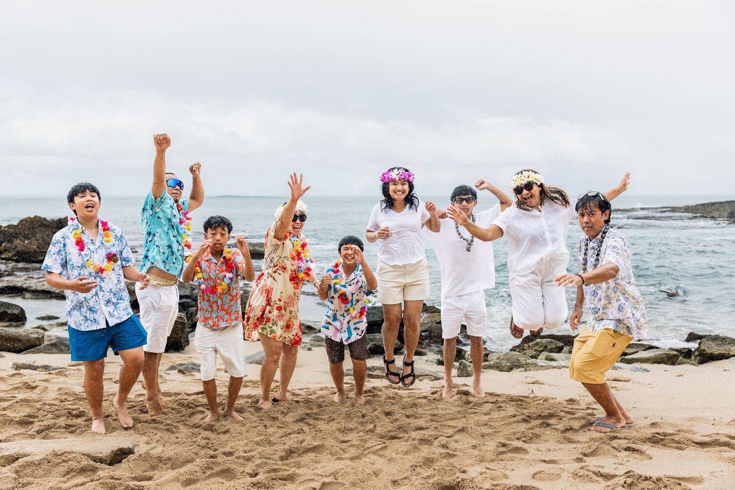 Group of joyful people jumping on a sandy beach in Hawaii, wearing colorful leis and tropical shirts.