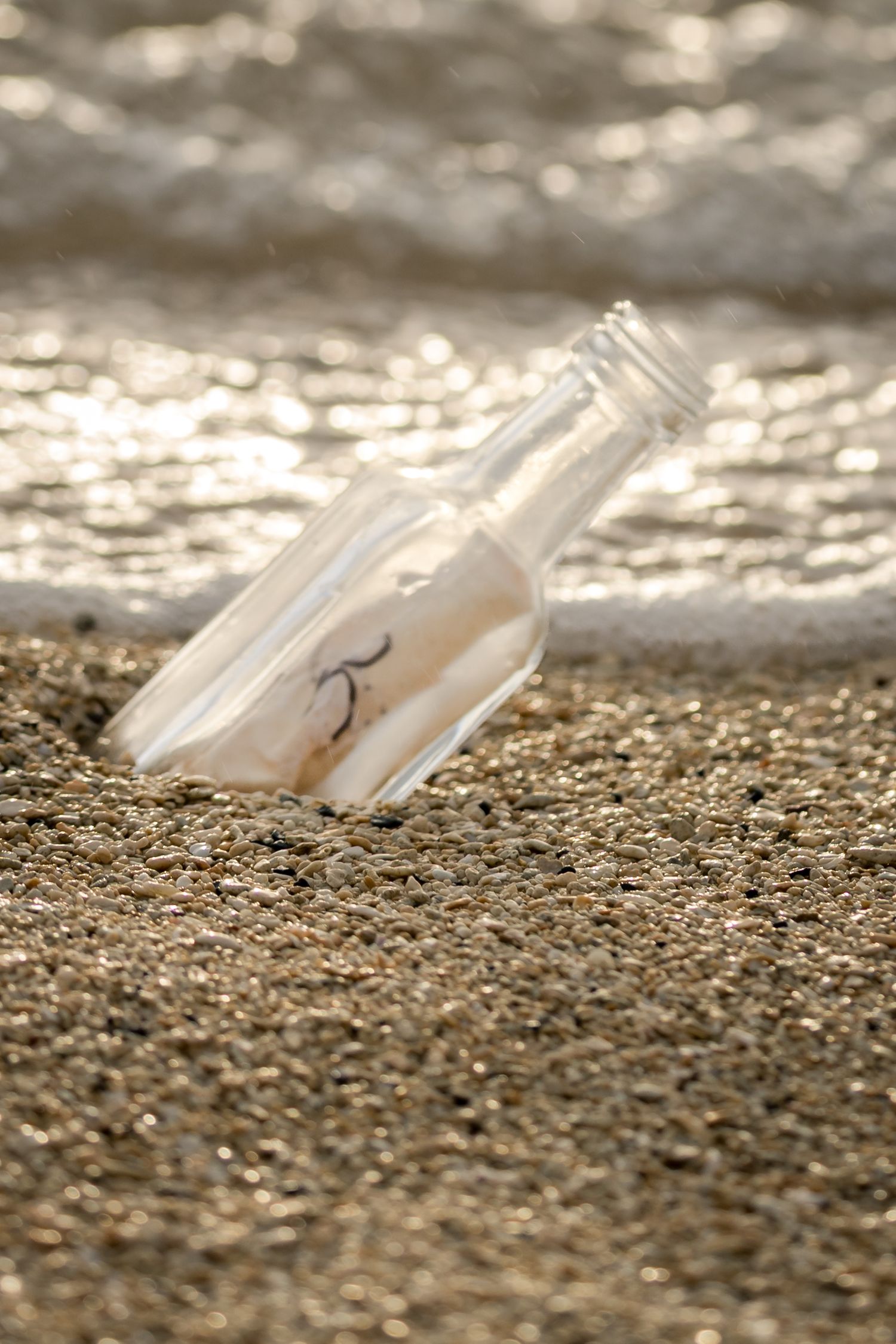 Glass bottle with message inside resting on sandy beach with ocean waves in background.