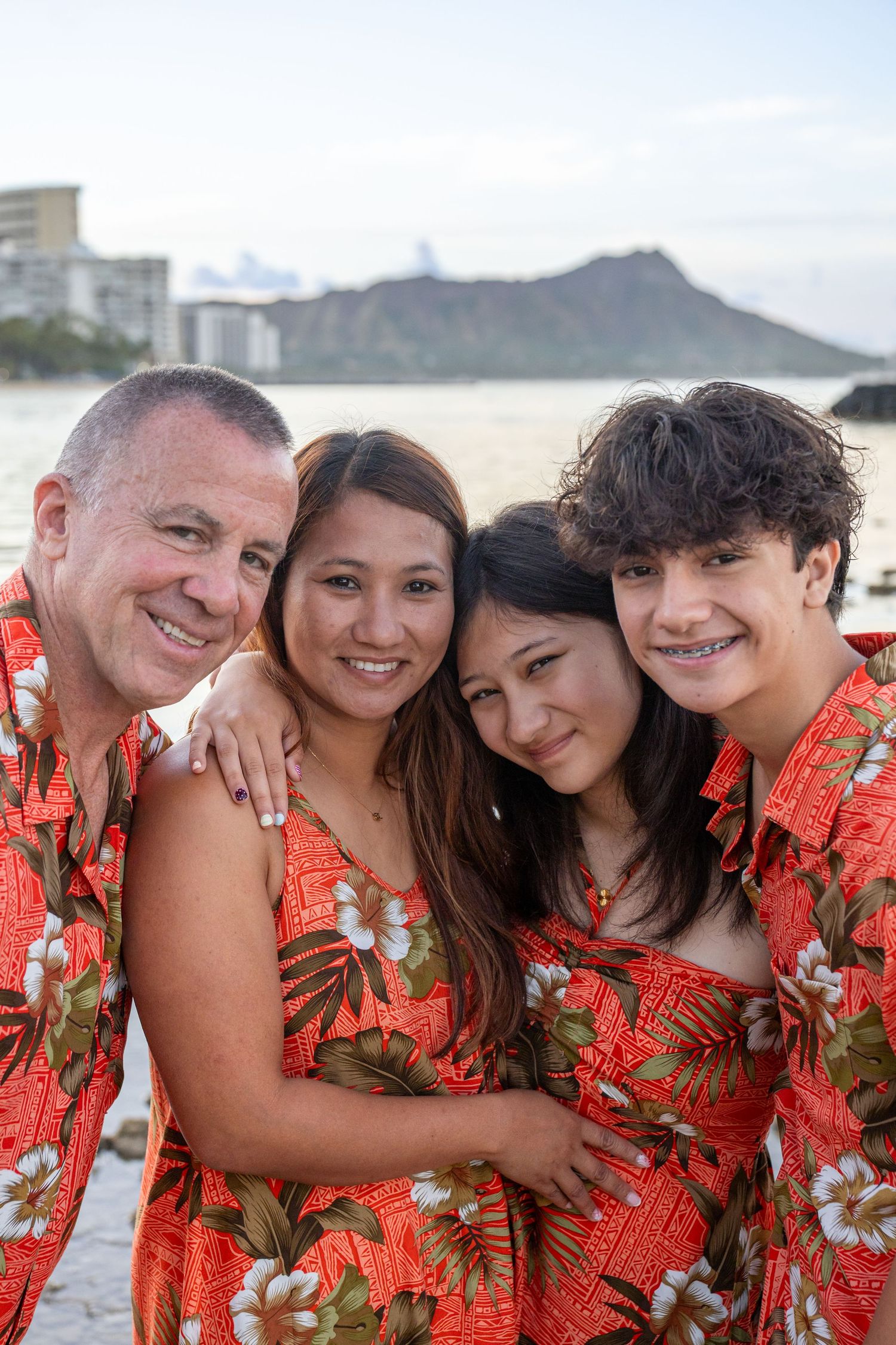 Family of four in matching red Hawaiian shirts posing at Waikiki Beach with Diamond Head.