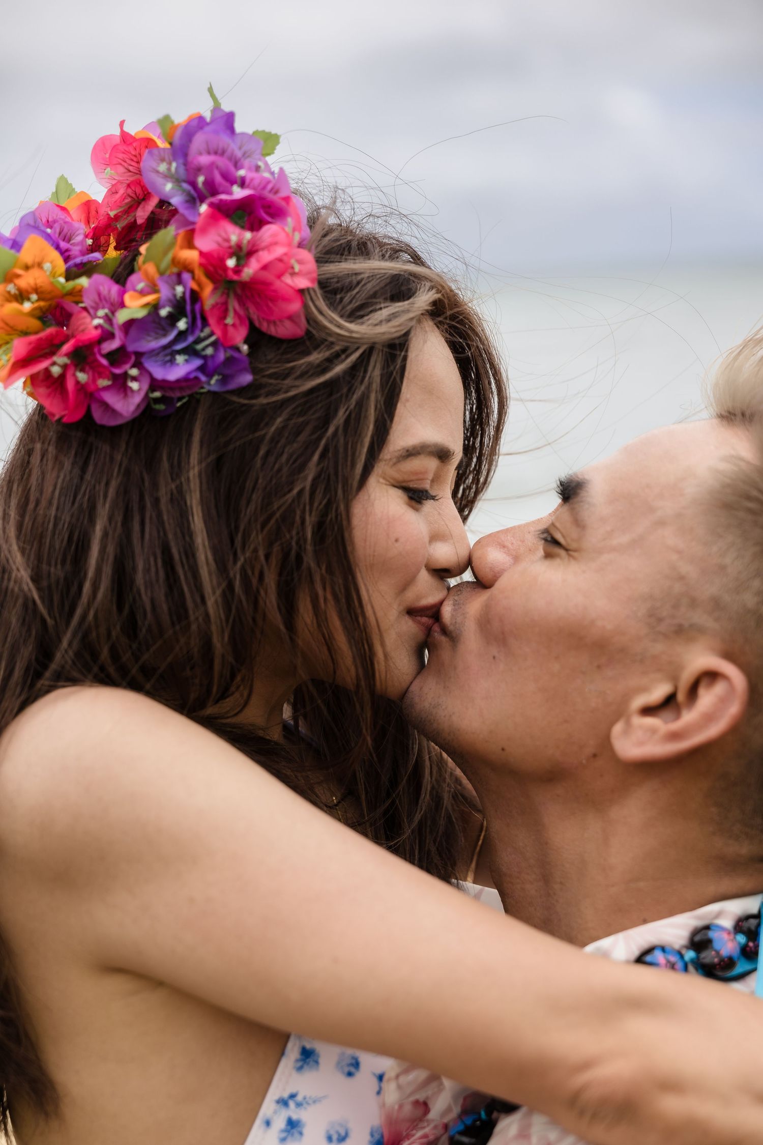 Couple sharing a romantic kiss on the beach, woman wearing colorful tropical flower crown.