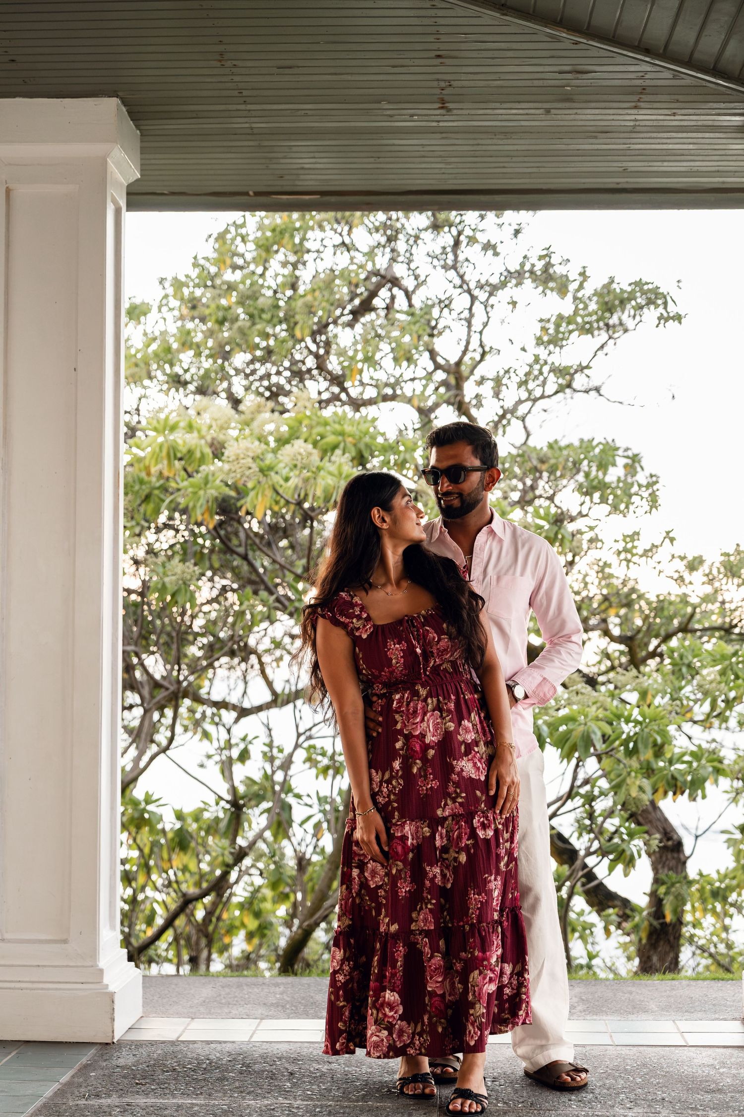 Couple posing romantically on a porch surrounded by lush tropical trees in Hawaii.