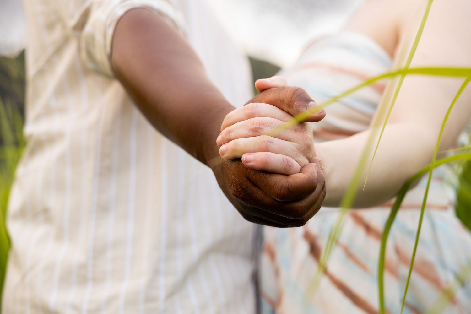 Interracial couple holding hands tenderly in a green outdoor setting.