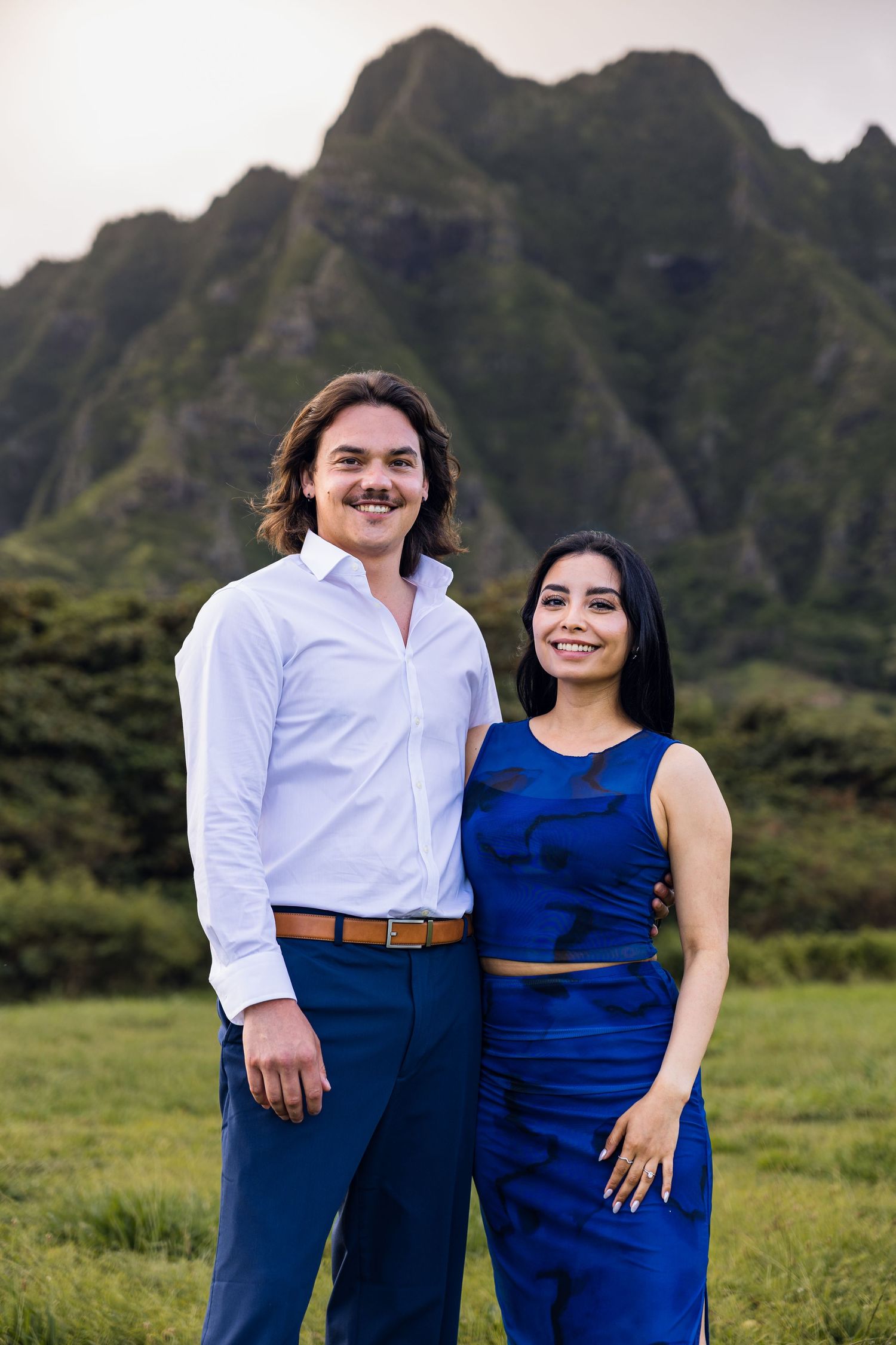 Couple posing together in blue outfits with lush green mountains in the background in Hawaii.