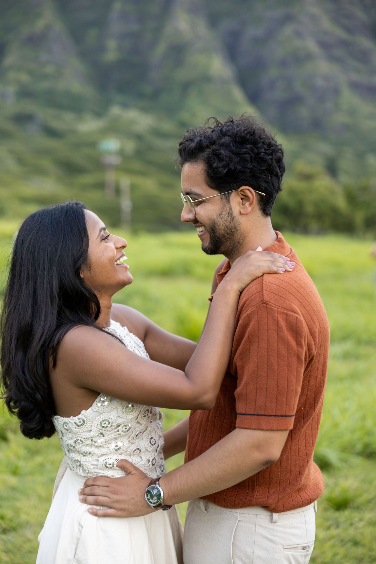 Smiling couple embracing in a green Hawaiian valley with dramatic mountains in the background.