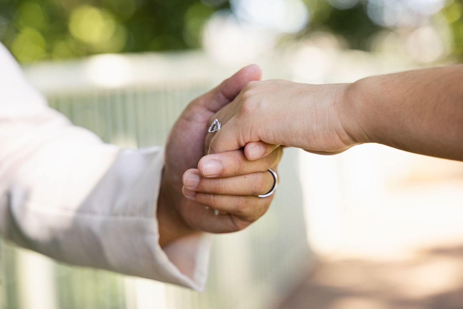 Close-up of a couple holding hands outdoors, with a silver wedding ring visible on one finger.