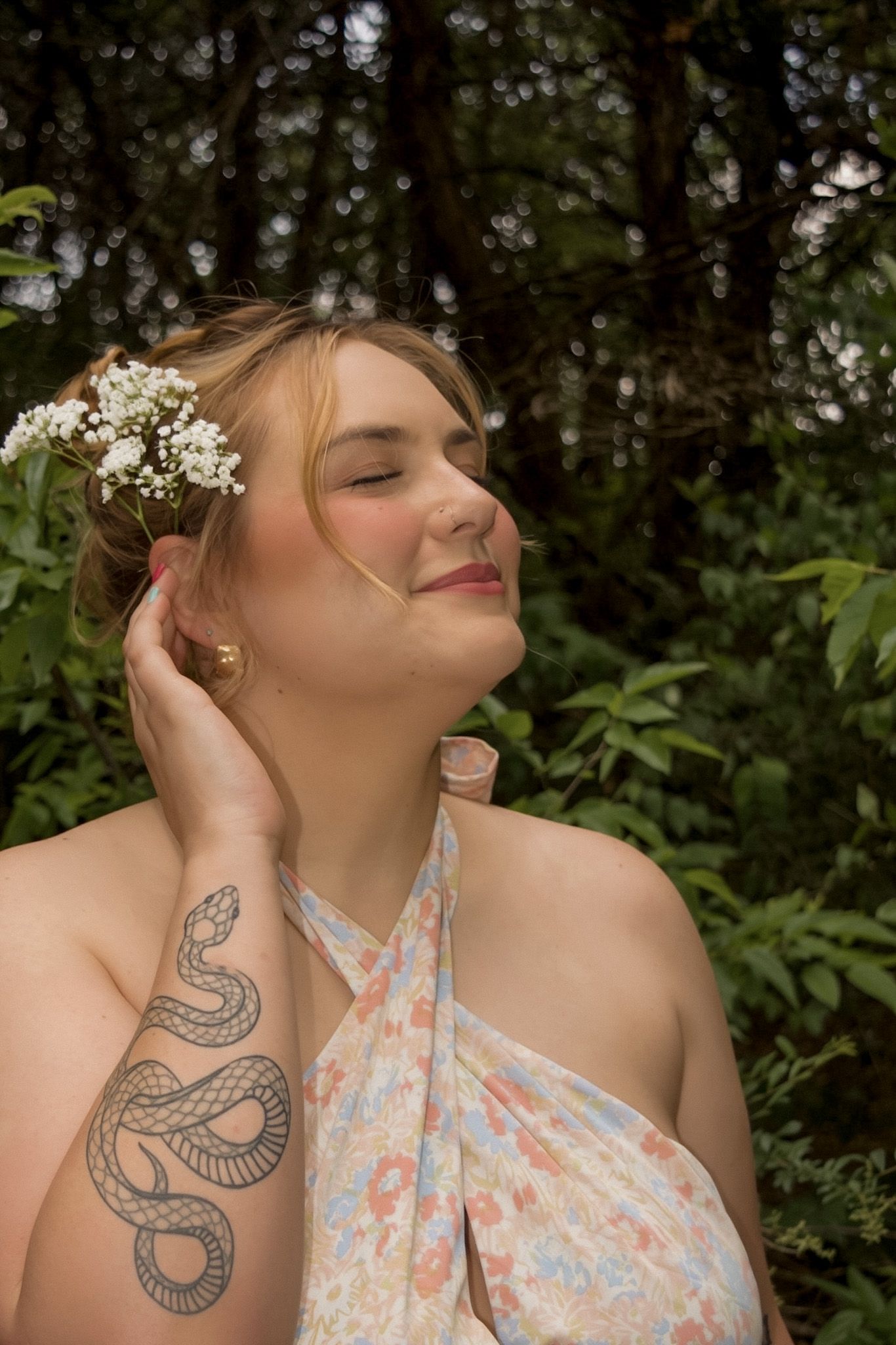 Plus-size woman with snake tattoo wearing floral halter dress and flower crown in forest setting.