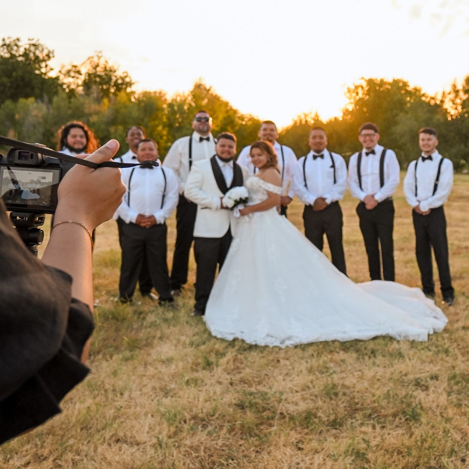 Photographer filming a wedding party with bride and groom and groomsmen in a golden field.