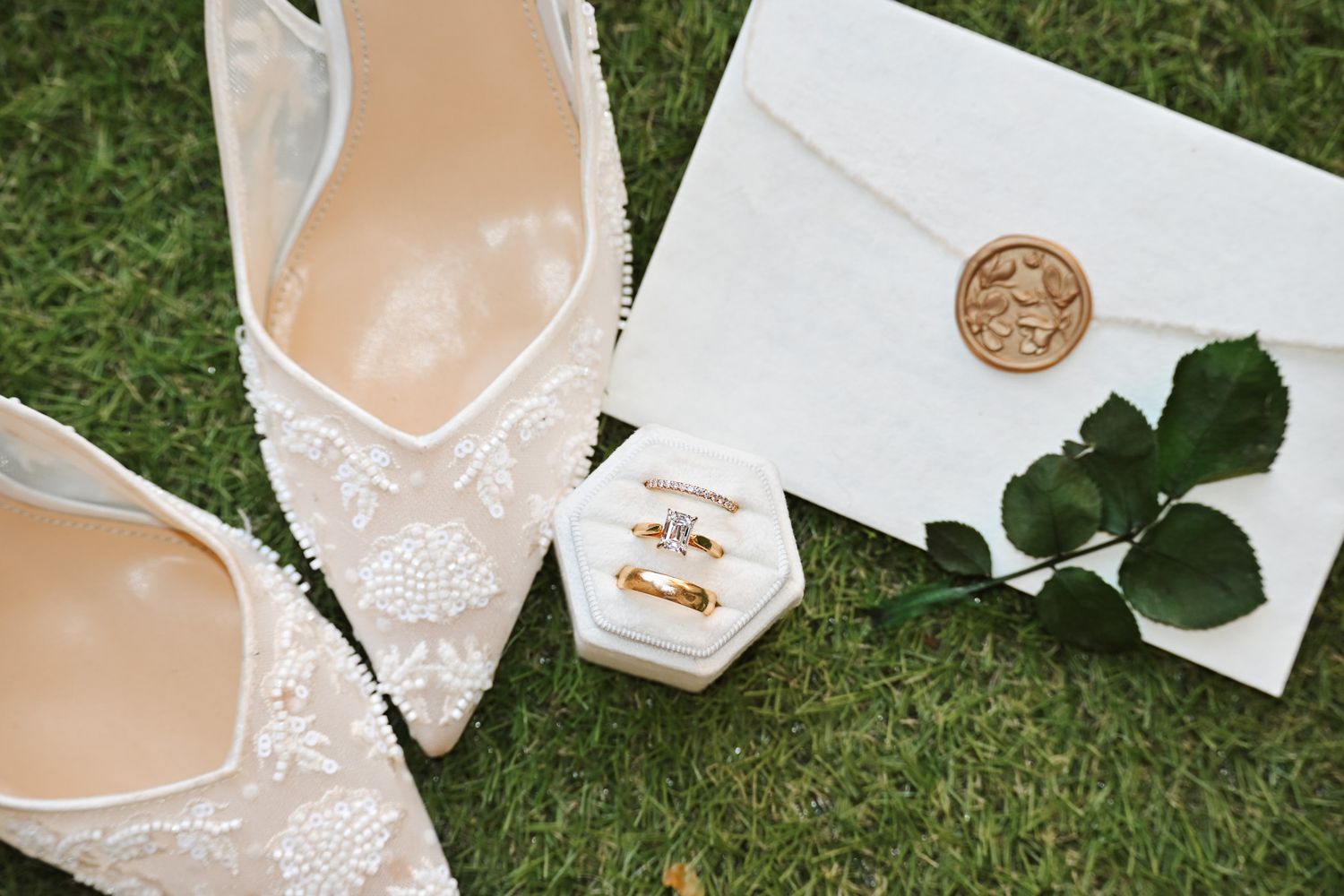 Wedding flat lay with lace bridal heels, gold rings in velvet box, and wax seal envelope.
