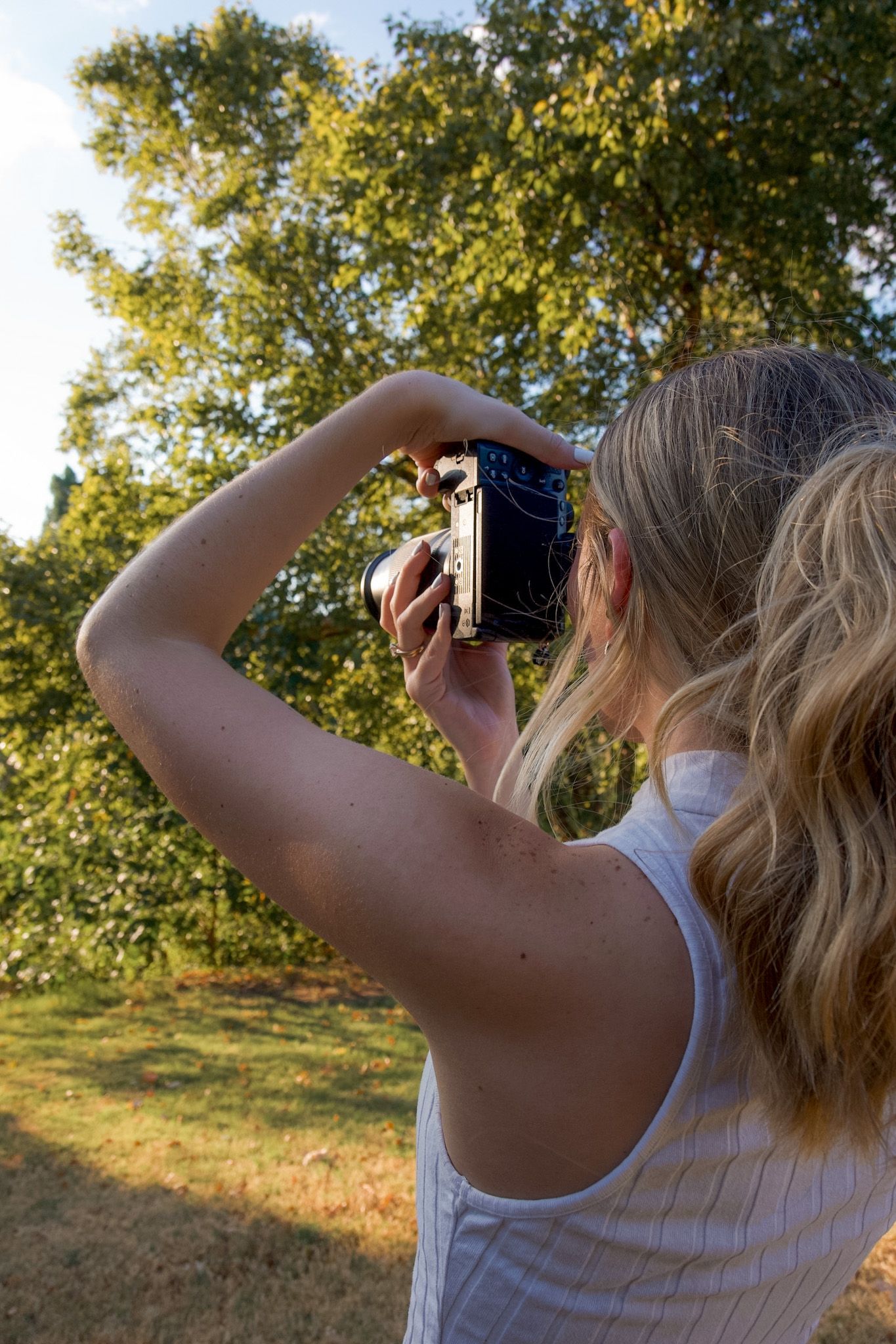 Young blonde woman capturing photos with a retro camera in a sunny green park.