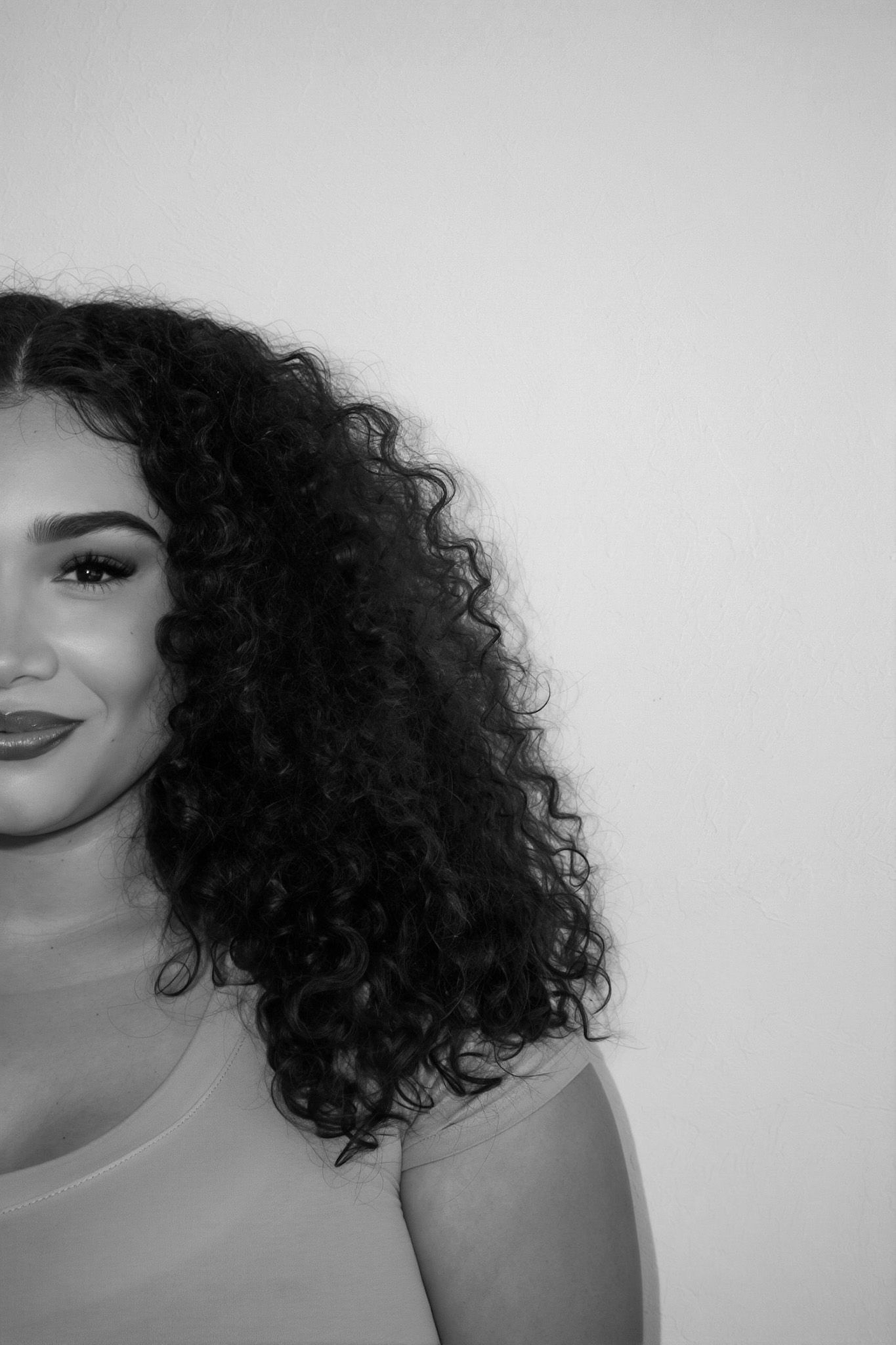 Black and white close-up portrait of a woman with voluminous curly hair and dark lipstick against a white background.