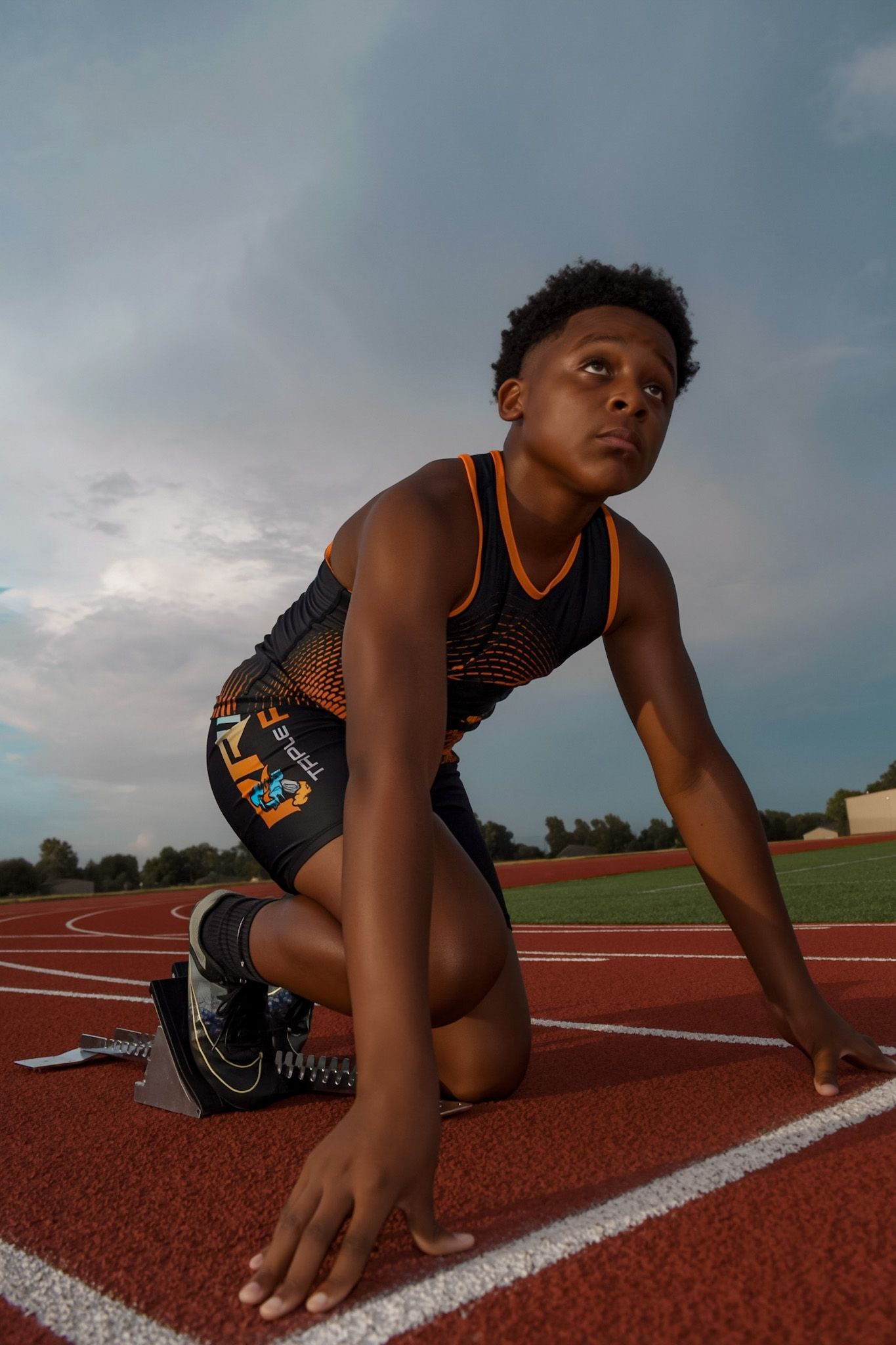 Young male track athlete in starting position on red running track under stormy sky.