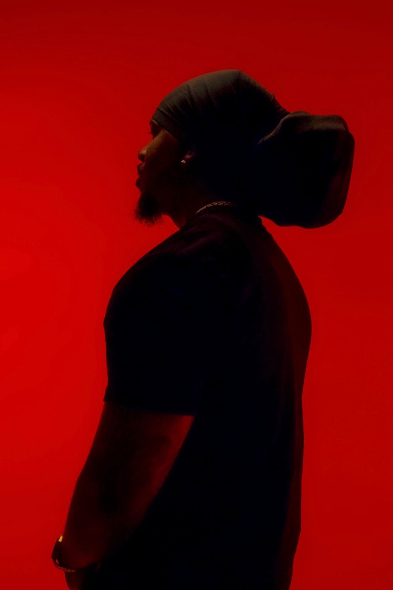 Dramatic silhouette profile of man wearing beanie against vibrant red background.