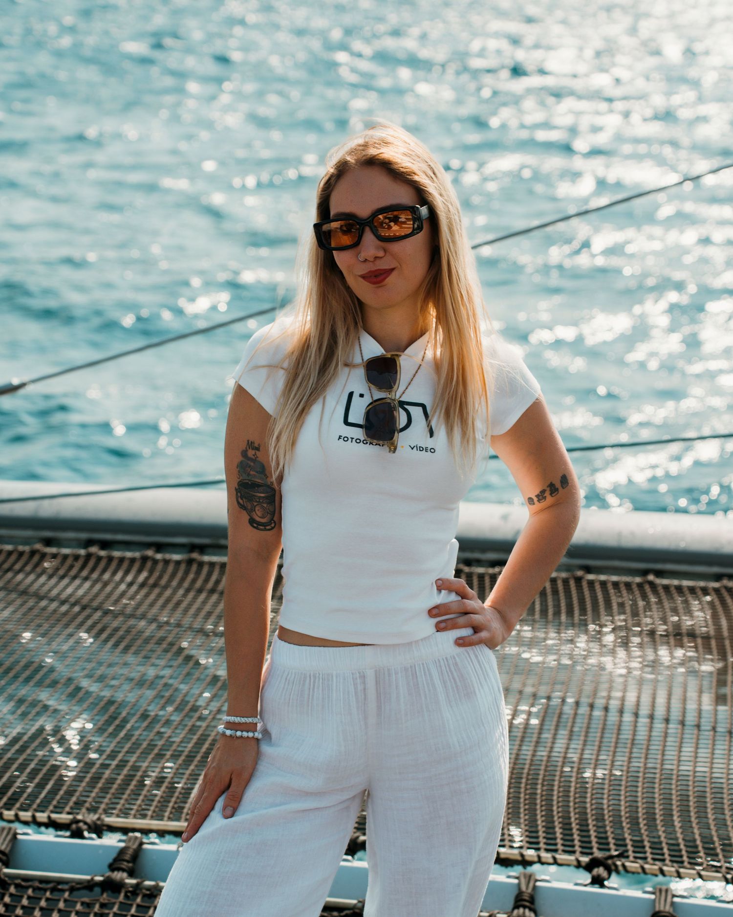 Mujer fotógrafa con ropa blanca y gafas de sol posando junto al mar