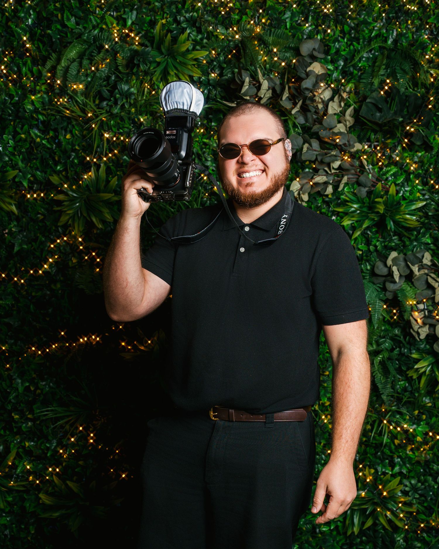 Retrato de un hombre fotógrafo con gafas de sol y camiseta negra rodeado de vegetación