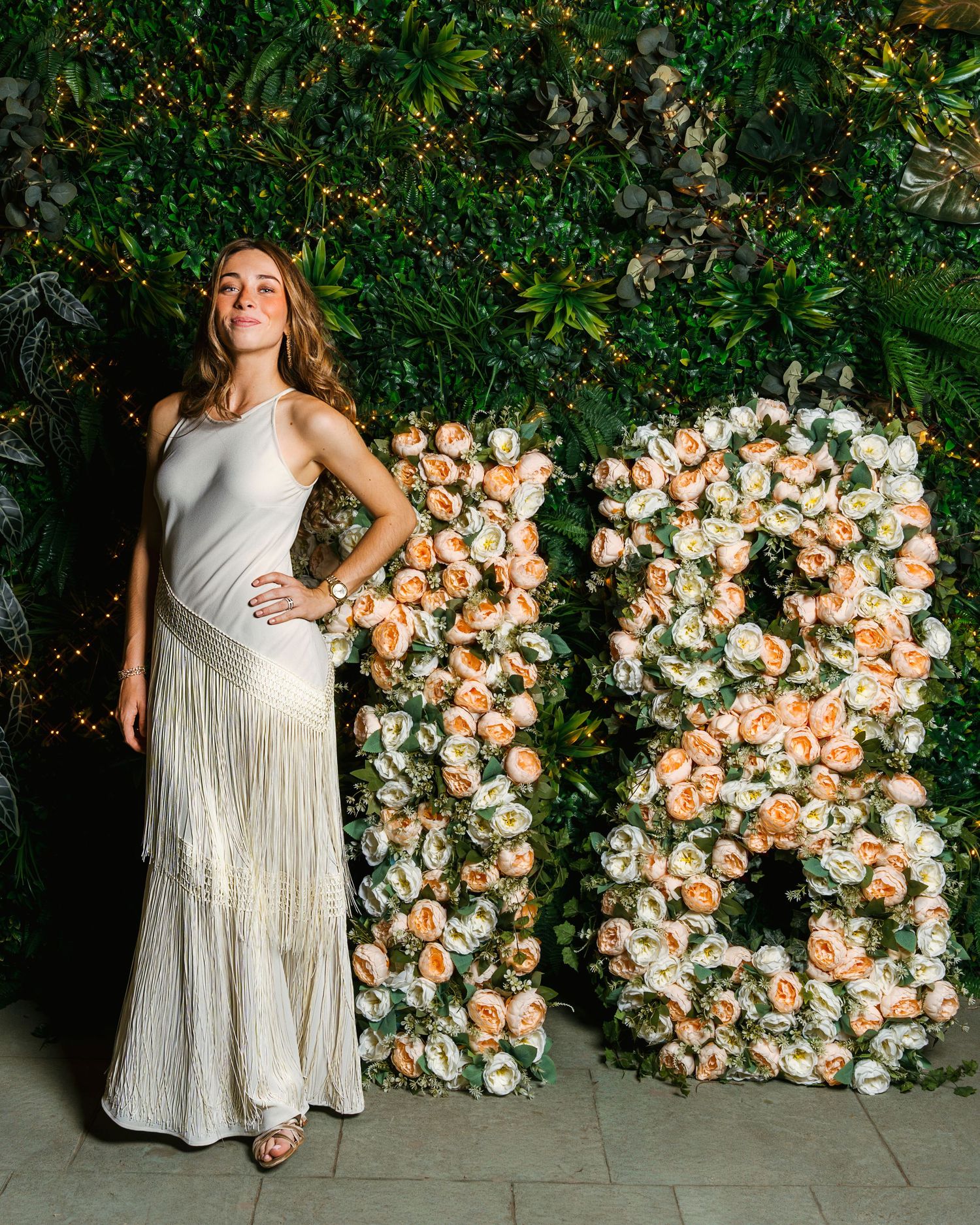 Retrato de una mujer con vestido largo blanco junto a una decoración floral