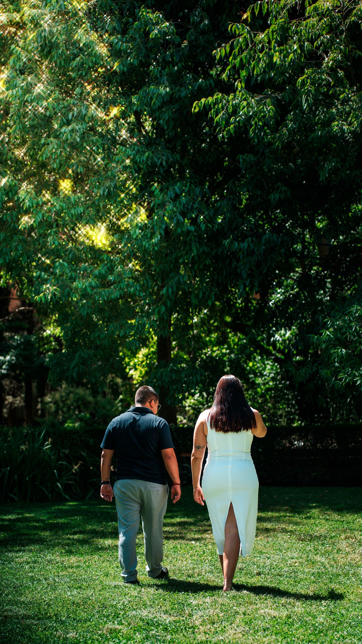 Pareja caminando de la mano por un jardín rodeado de árboles
