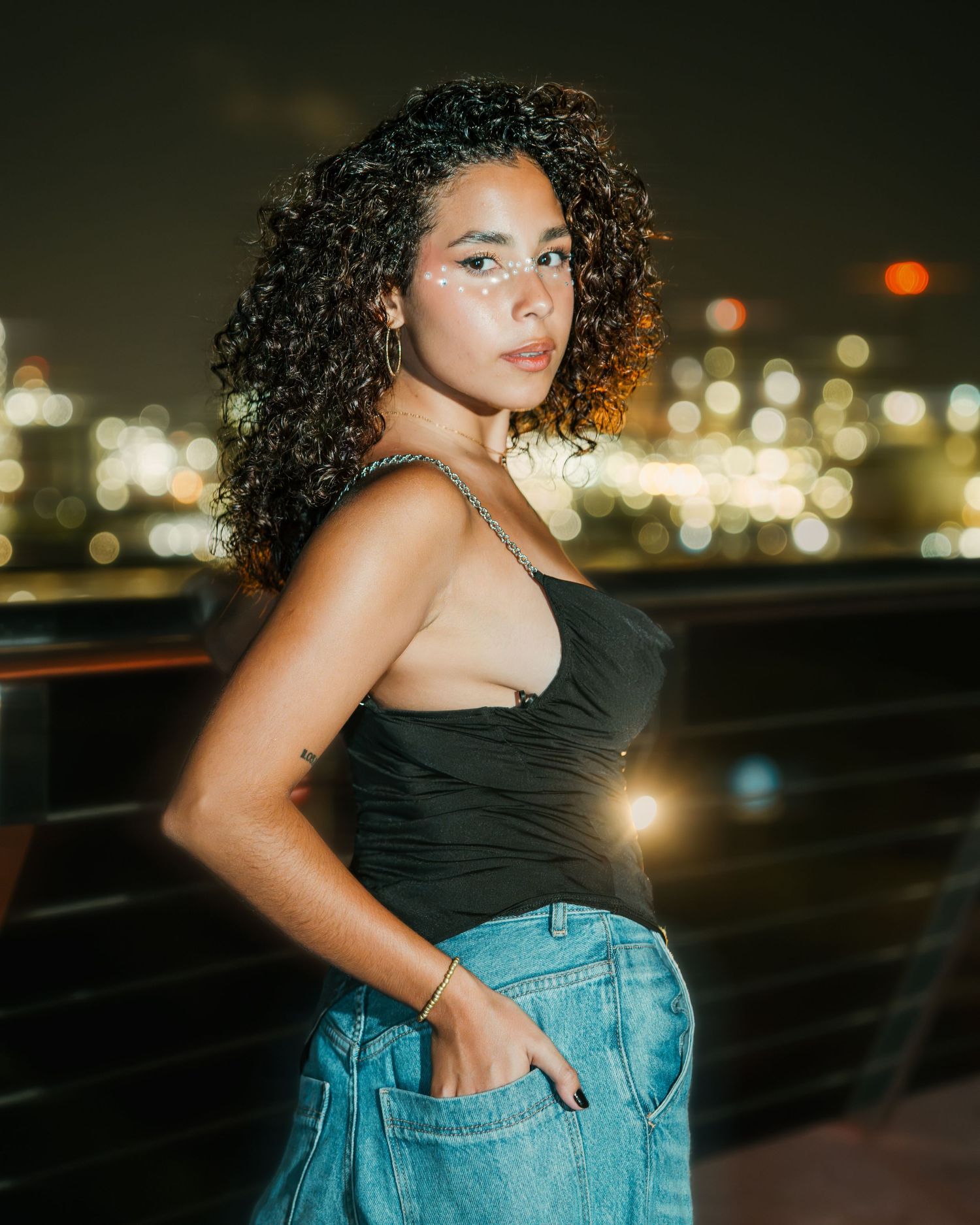 Retrato de una mujer con top negro y jean azul junto al mar de noche