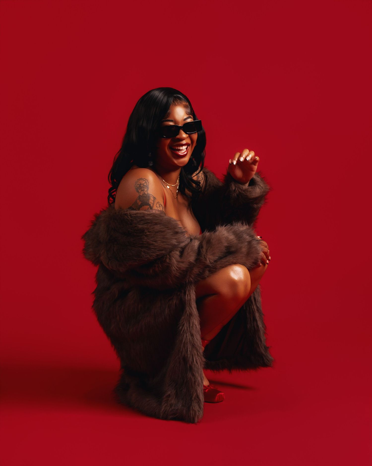 Woman in fur coat and sunglasses posing confidently against a bold red background.
