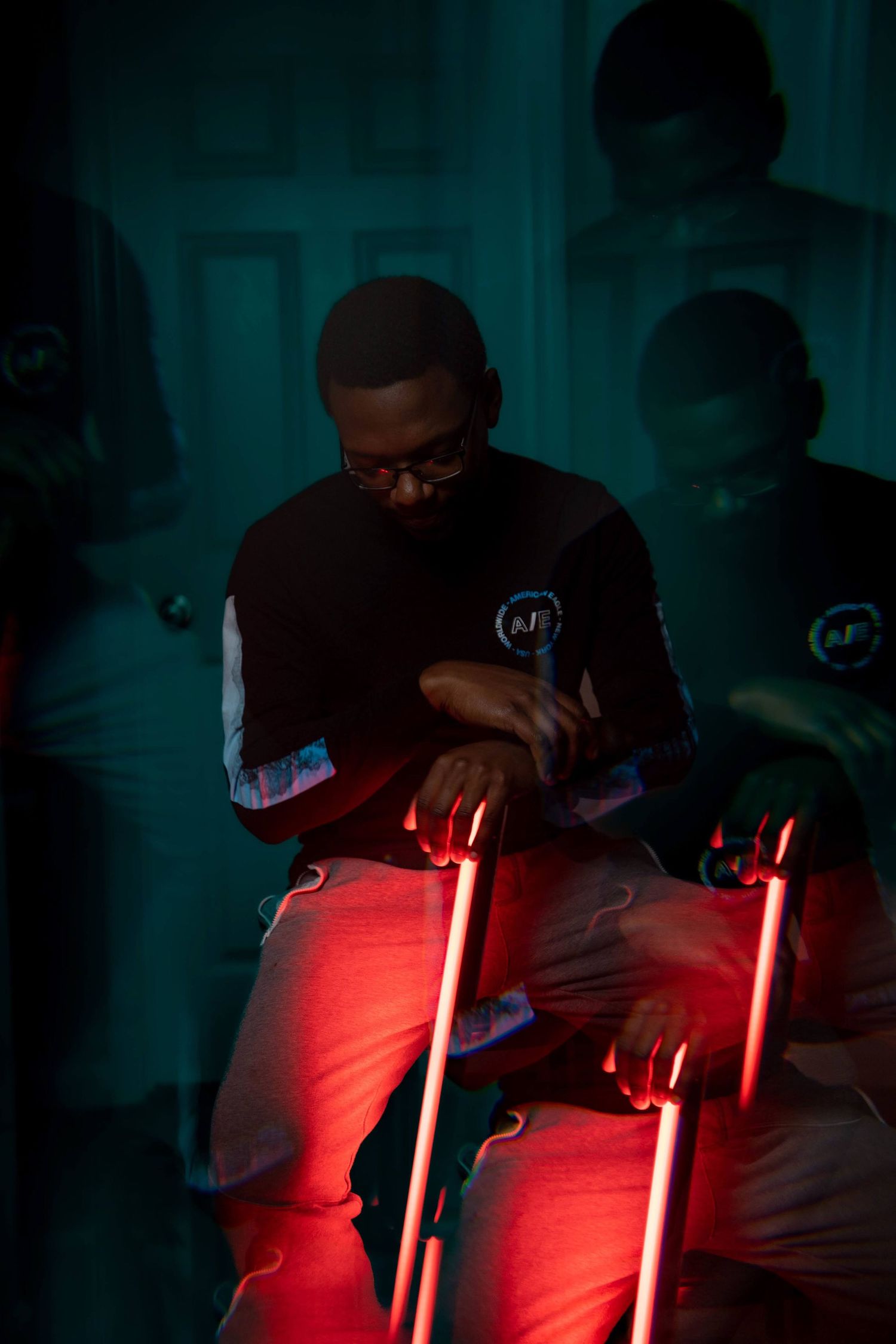 Man in glasses sitting with red neon lights in a dark teal-lit room.