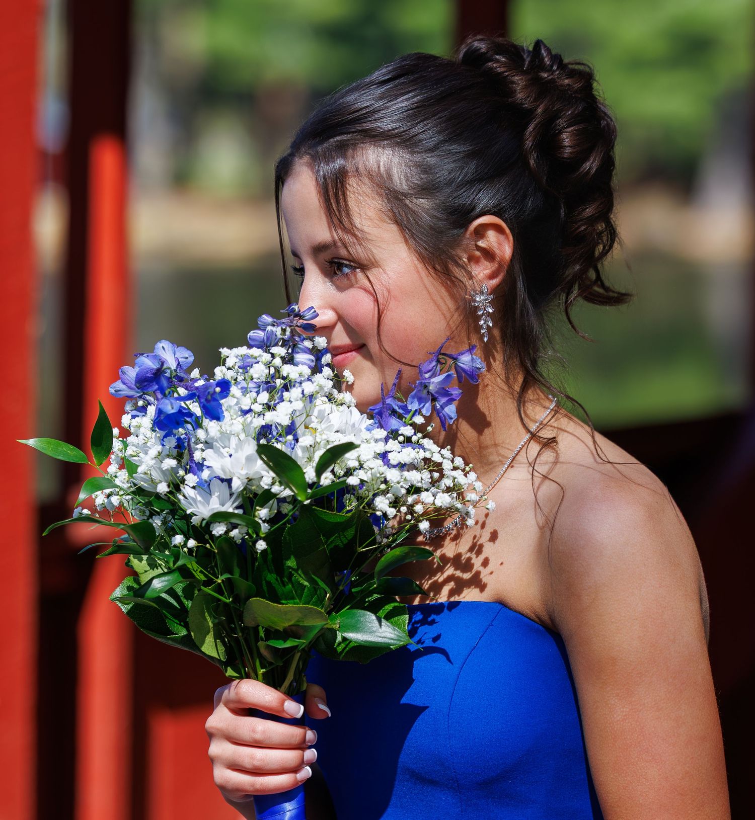 Young woman in blue dress smelling a bouquet of blue and white flowers outdoors.