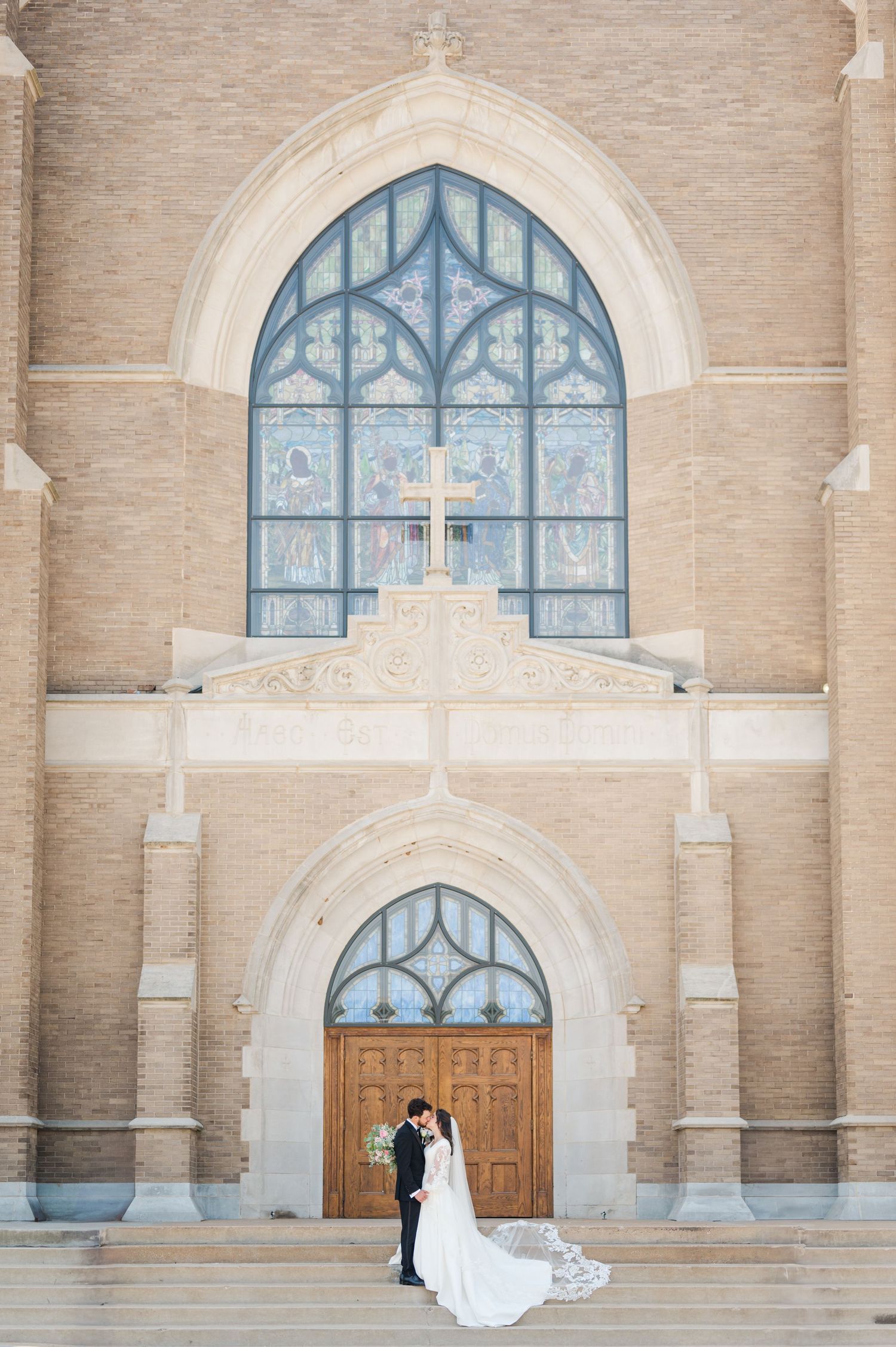 Bride and groom pose on the steps of Holy Family Cathedral in Tulsa, Oklahoma after their wedding.